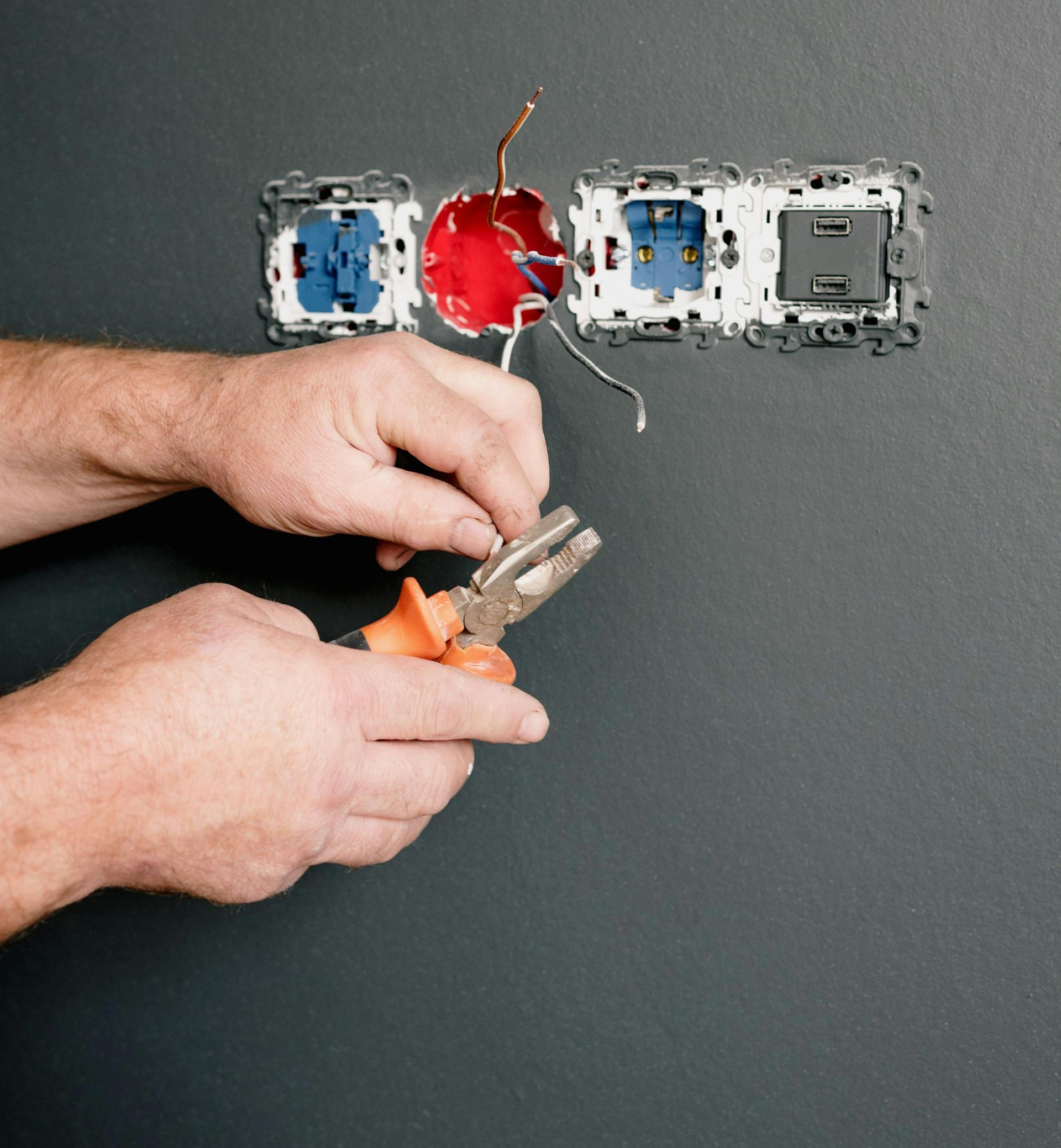 Person using pliers to work on electrical wiring in a wall.