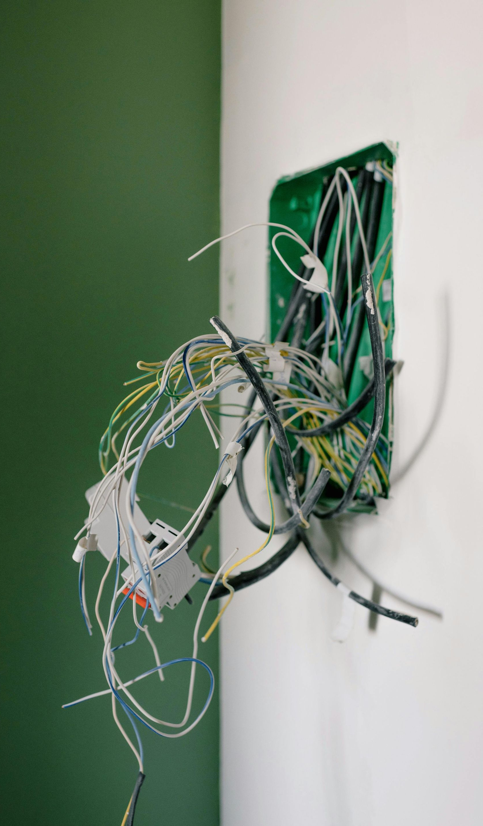 Electrical wires spilling from a green junction box on a white wall; green wall to the left.