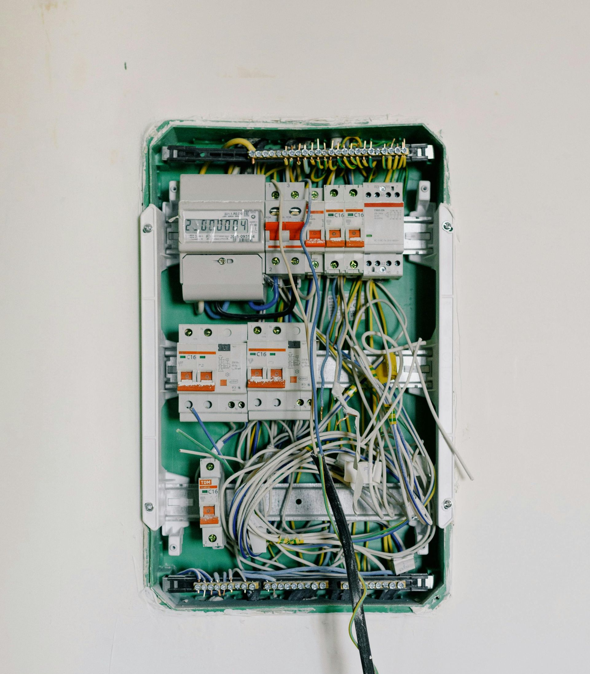 Electrical panel with wires and circuit breakers, recessed in a white wall.