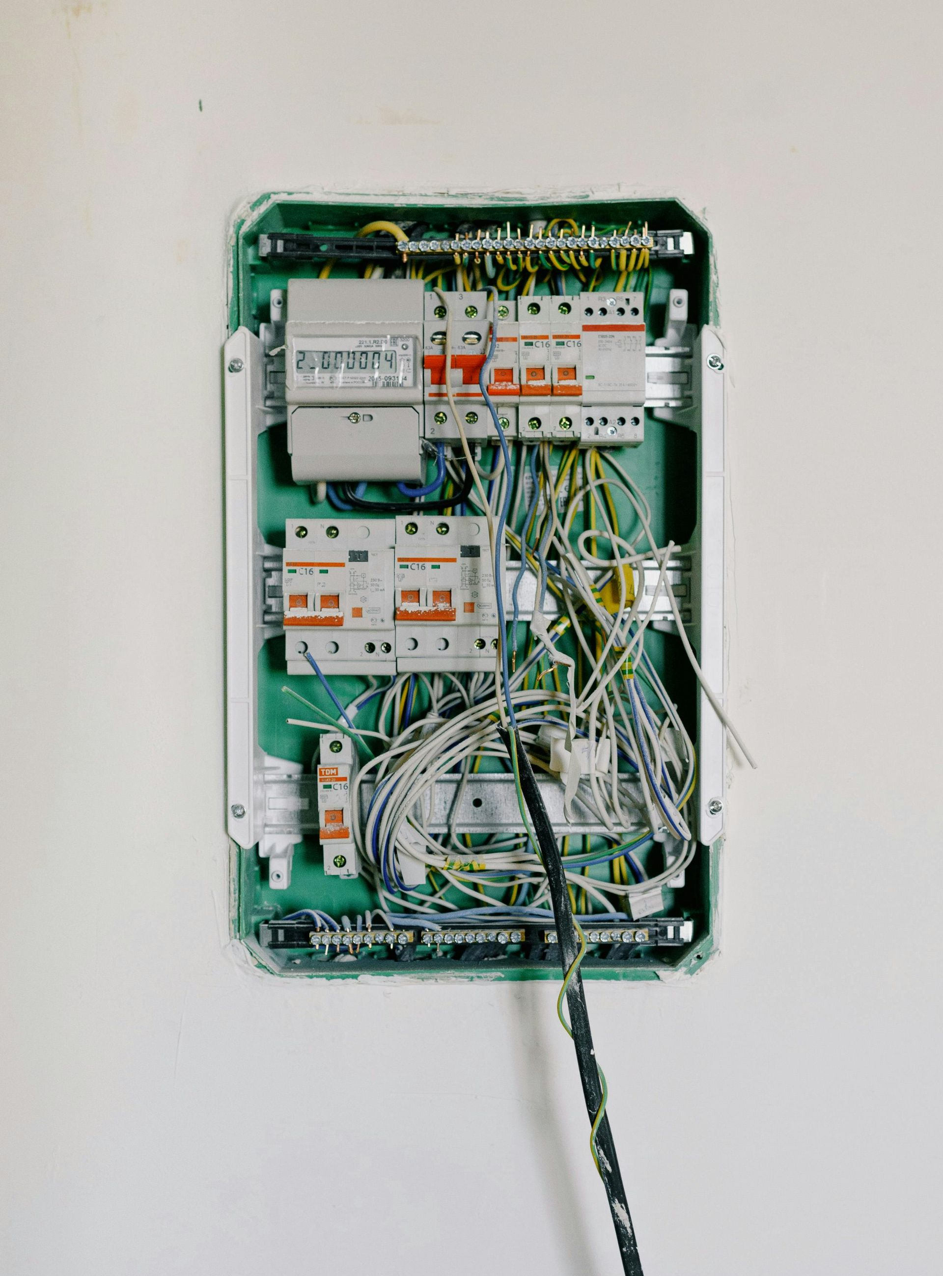 Open electrical panel with wires and circuit breakers, installed in a white wall.