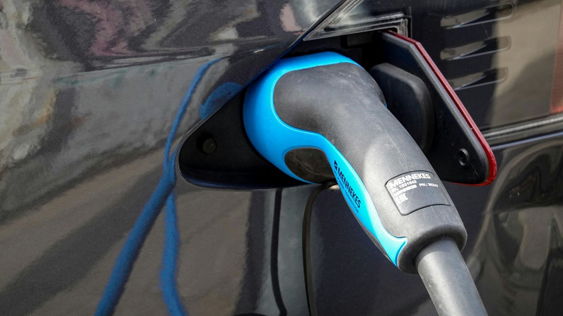 An electric vehicle charging port with a blue and black charging cable plugged in.