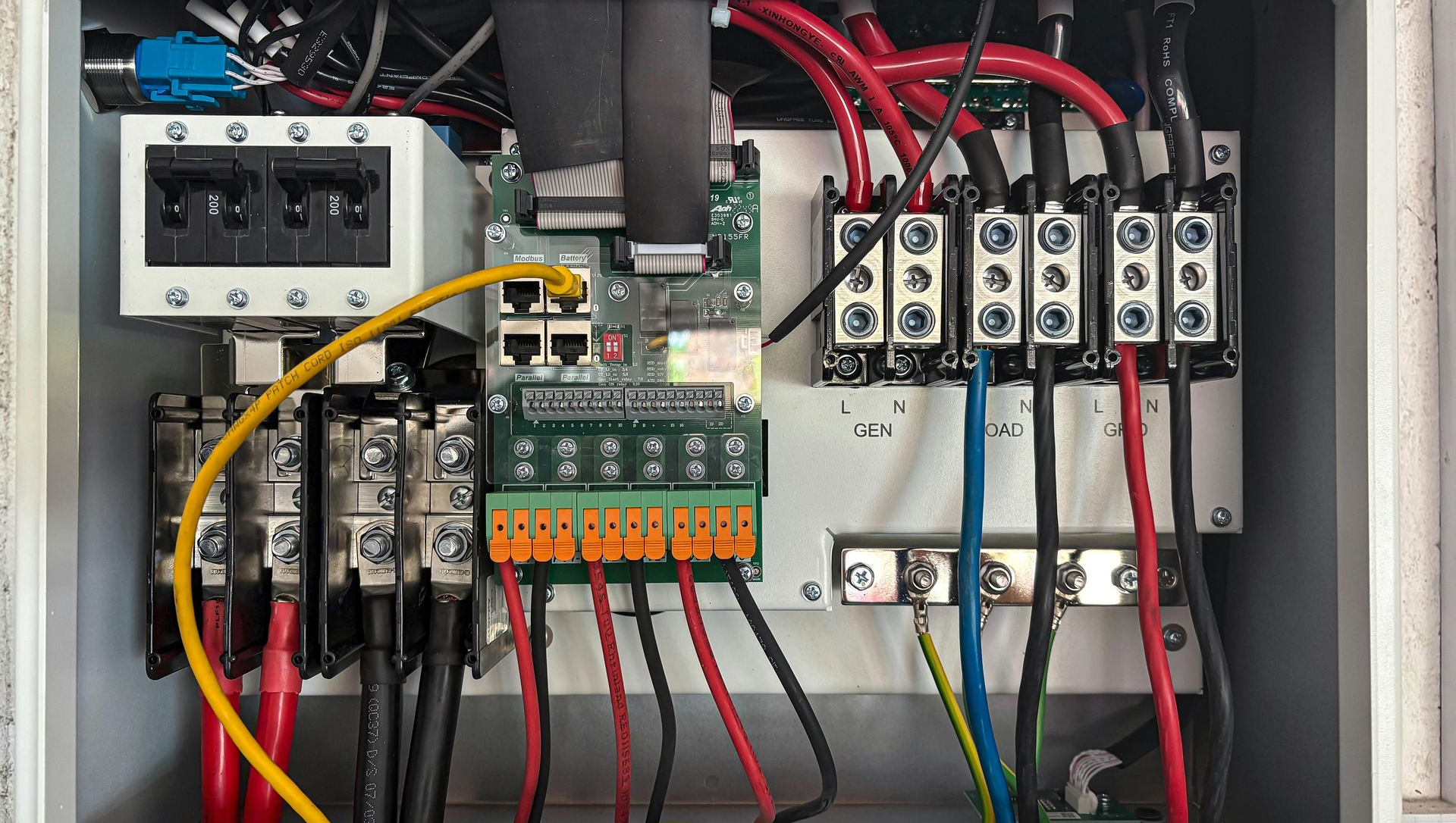 Electrical control panel with wires, breakers, and circuit board inside a white box.