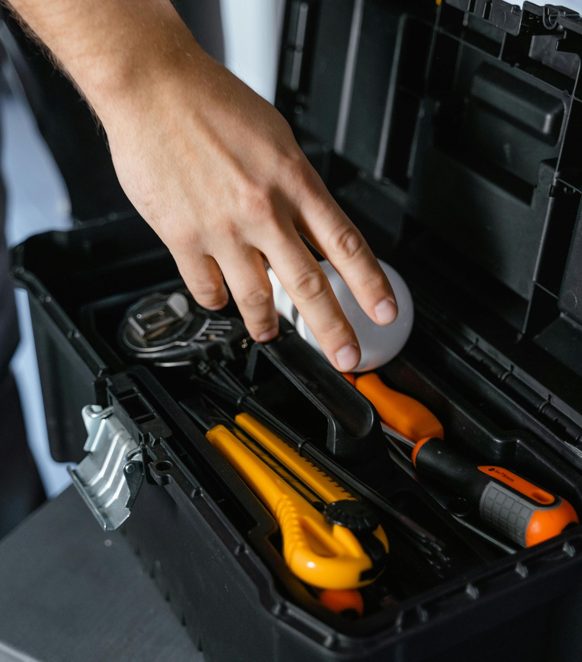 Hand reaching for a lightbulb in a toolbox with yellow and orange tools.
