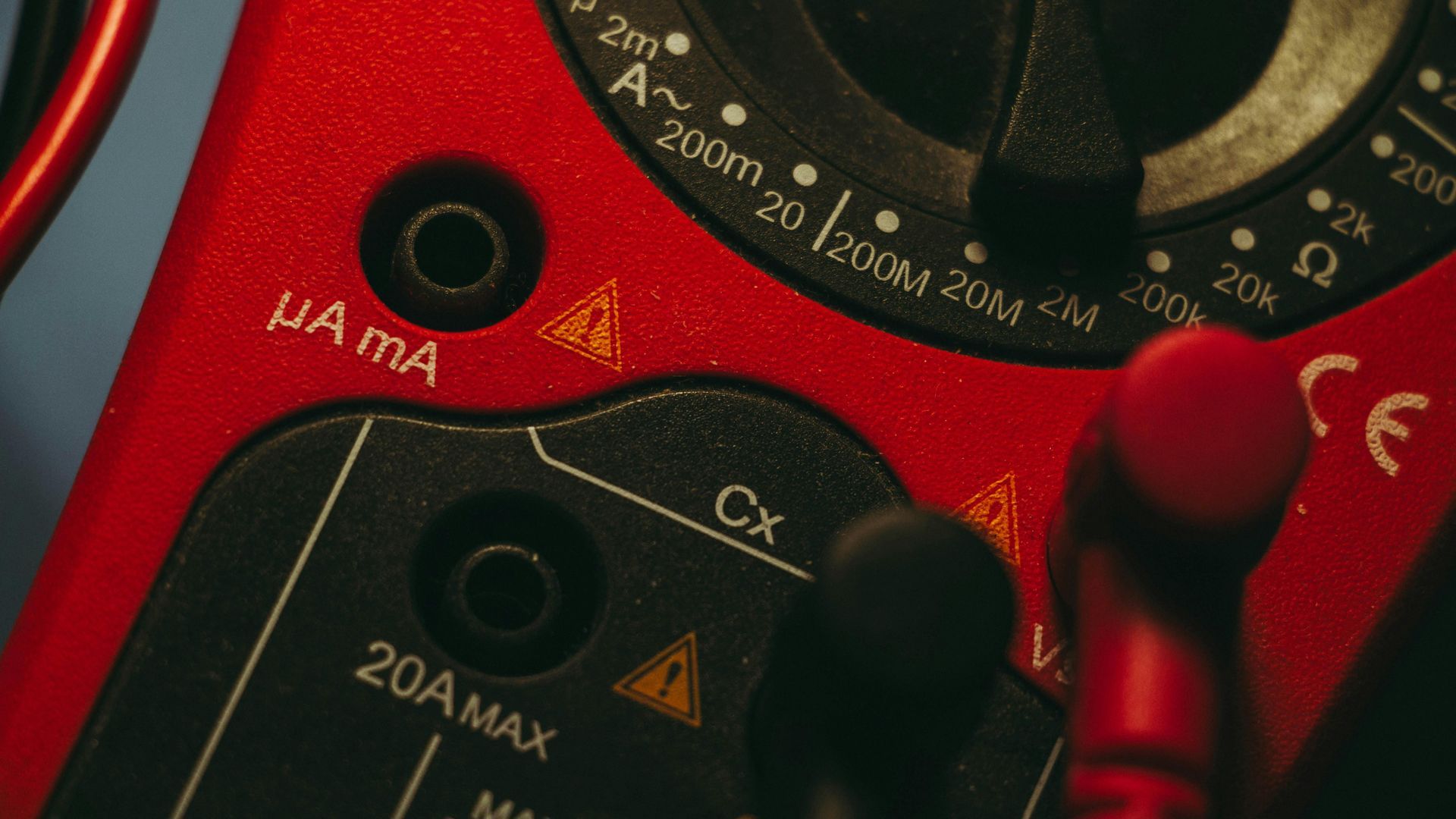 Close-up of a red multimeter dial with black probes, showing settings for current and resistance.