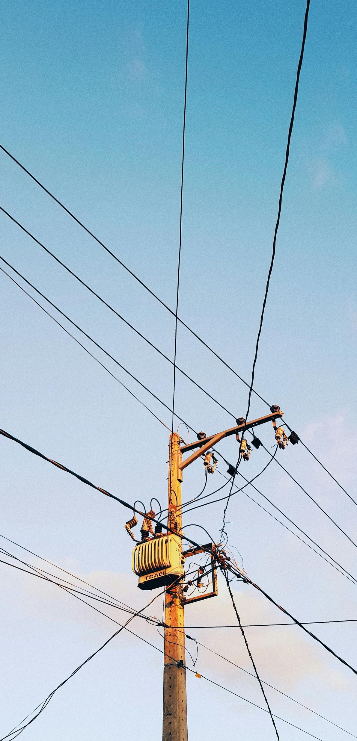 Utility pole with electrical transformer and wires against a blue sky.