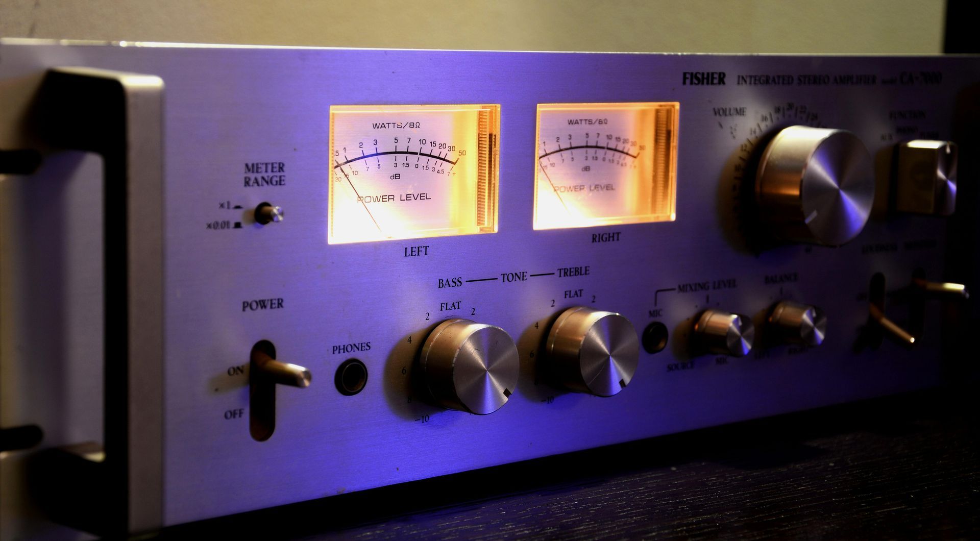 Silver audio amplifier with illuminated meters and control knobs.