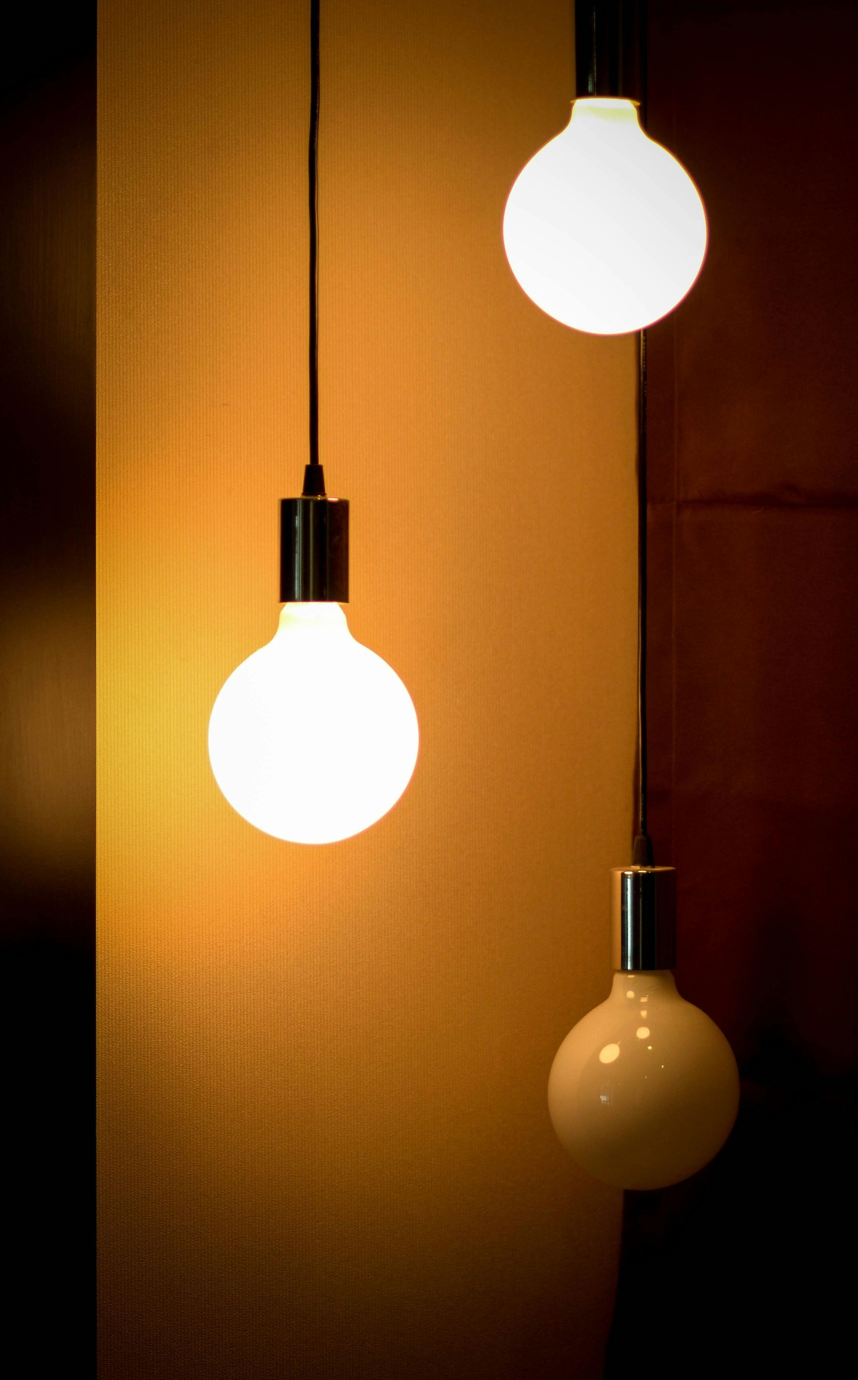 Three glowing spherical light bulbs hanging from the ceiling, illuminating a warm-toned wall.