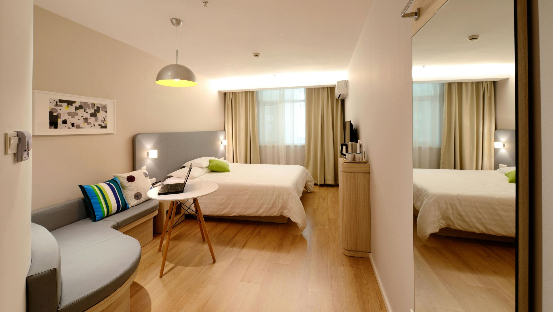 Modern hotel room with a bed, bench, and a full-length mirror.