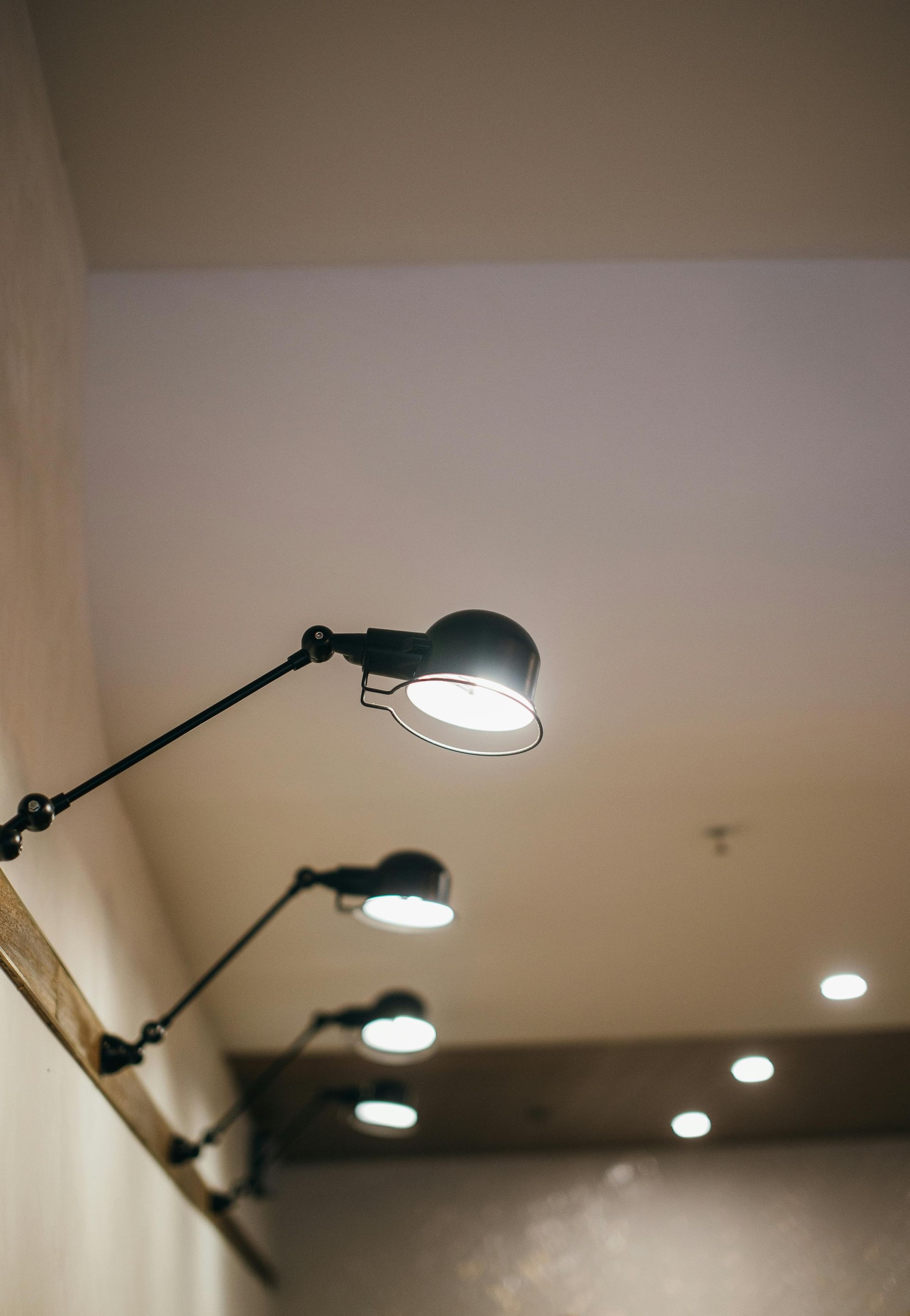 Black wall-mounted lamps illuminating a light-colored ceiling and wooden beam.