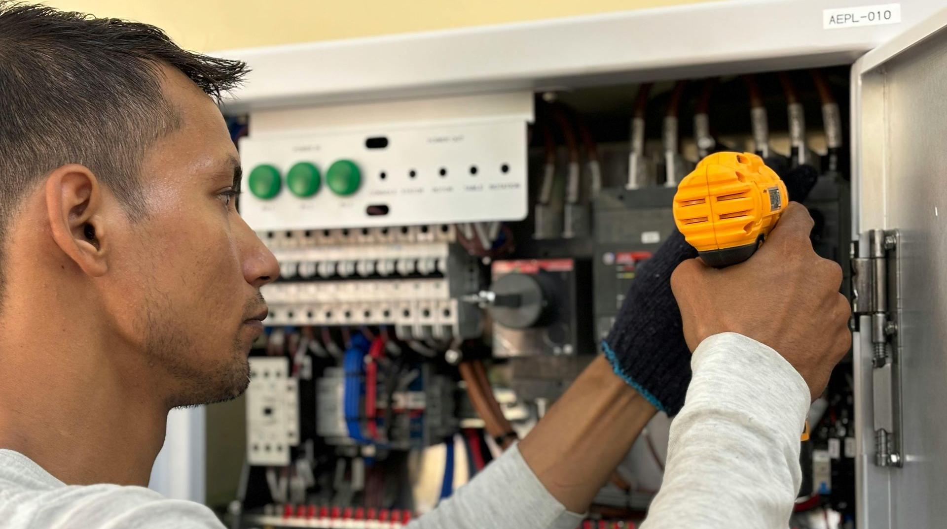 Man working on electrical panel with tool, wearing gloves.