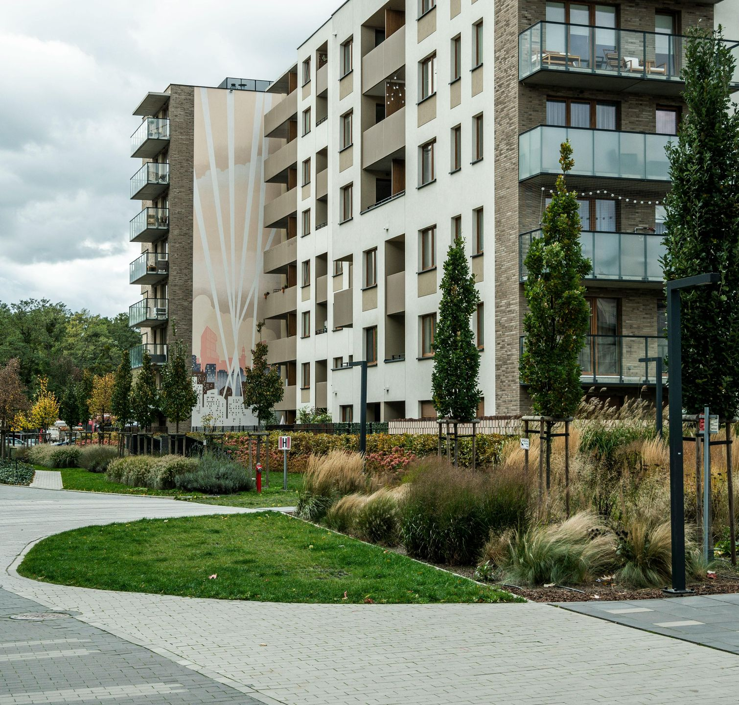 Modern apartment building with balconies, landscaped grounds, and cloudy sky.