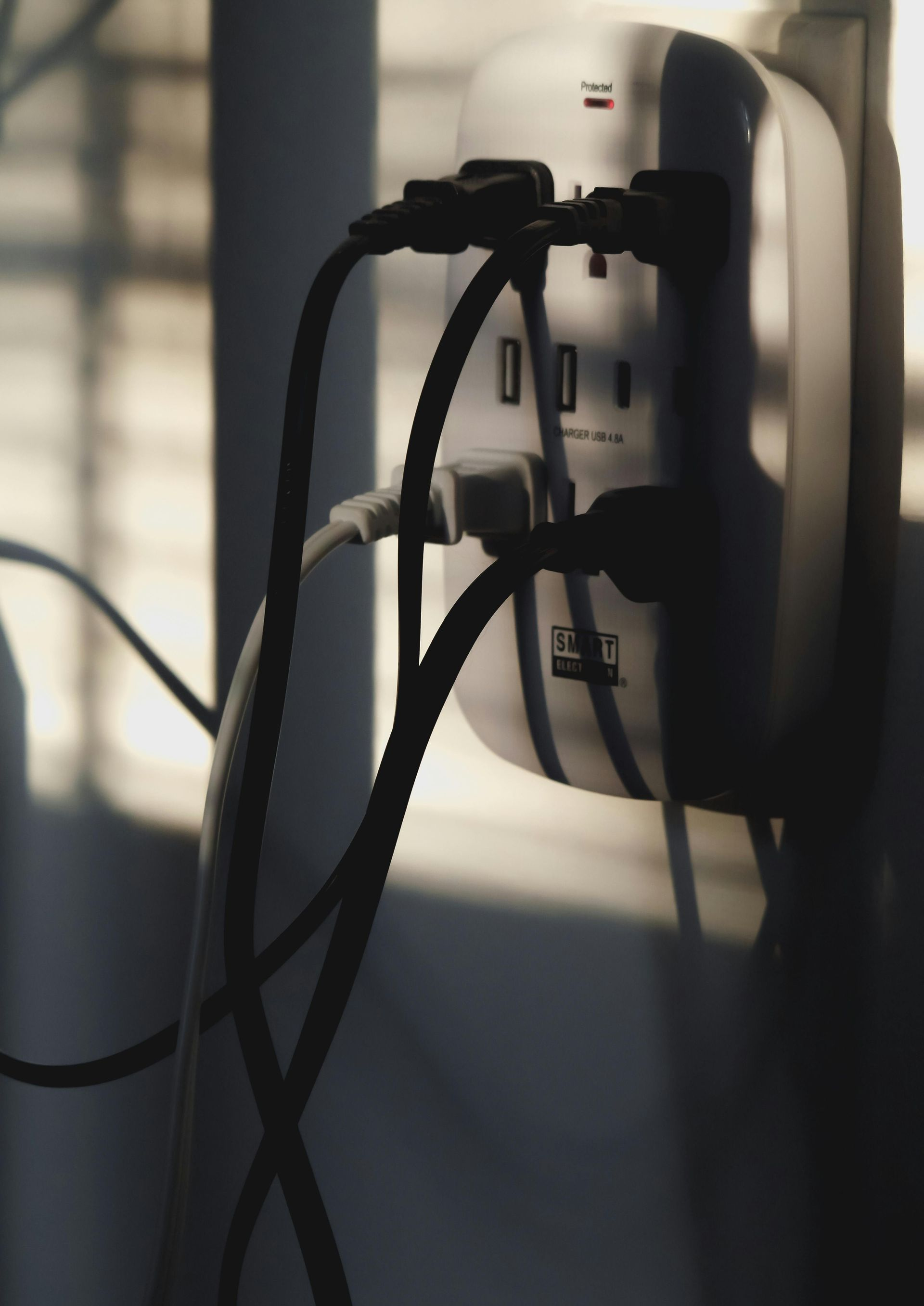 White power strip with multiple cords plugged in, against a wall, lit by sunlight.