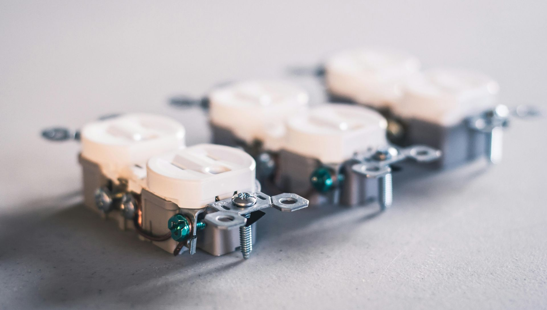 Three electrical outlets, white and silver, with mounting brackets, resting on a gray surface.