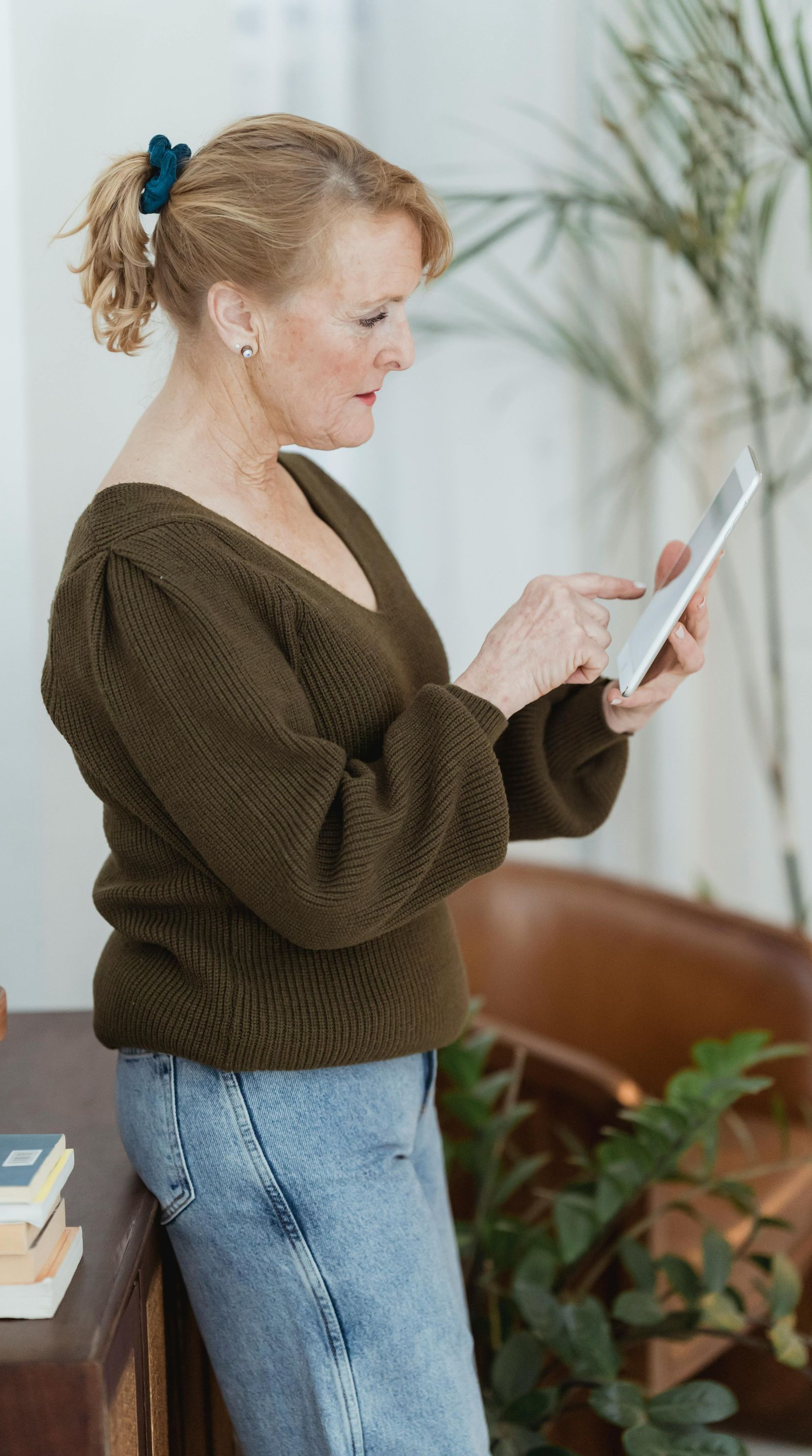 A person in a dark green knit sweater leans against a table while using a tablet.