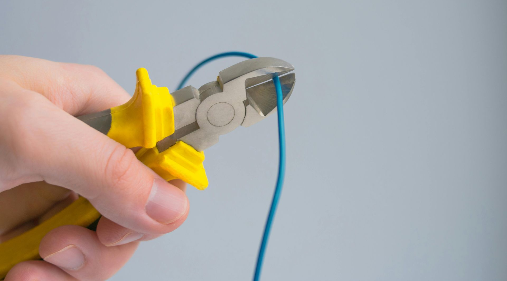 Hand cutting a blue wire with yellow and gray wire cutters.