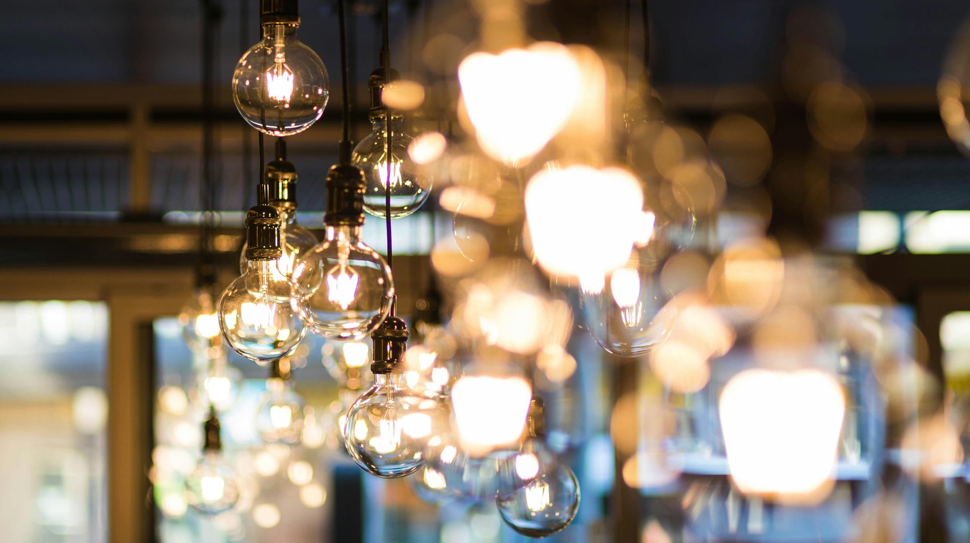Several lit, clear glass Edison light bulbs hanging from the ceiling, blurred background.