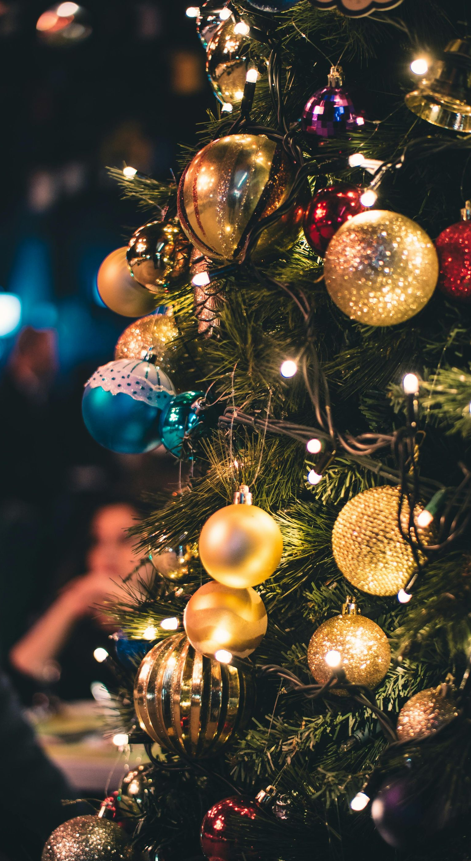 Christmas tree adorned with gold, blue, and red ornaments, lit by white string lights.