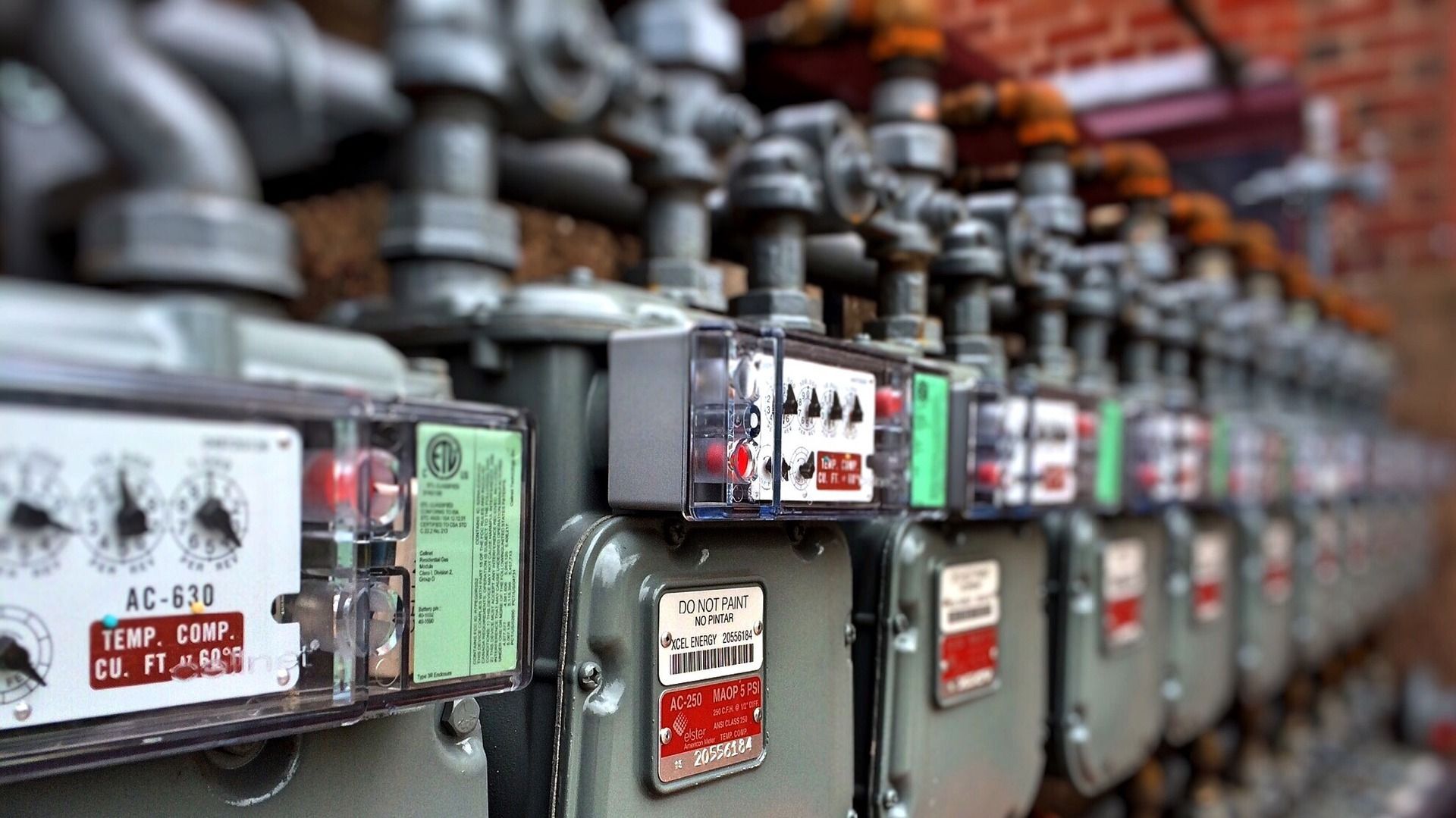 Row of gray gas meters attached to a brick wall. Each has a clear, boxed display.
