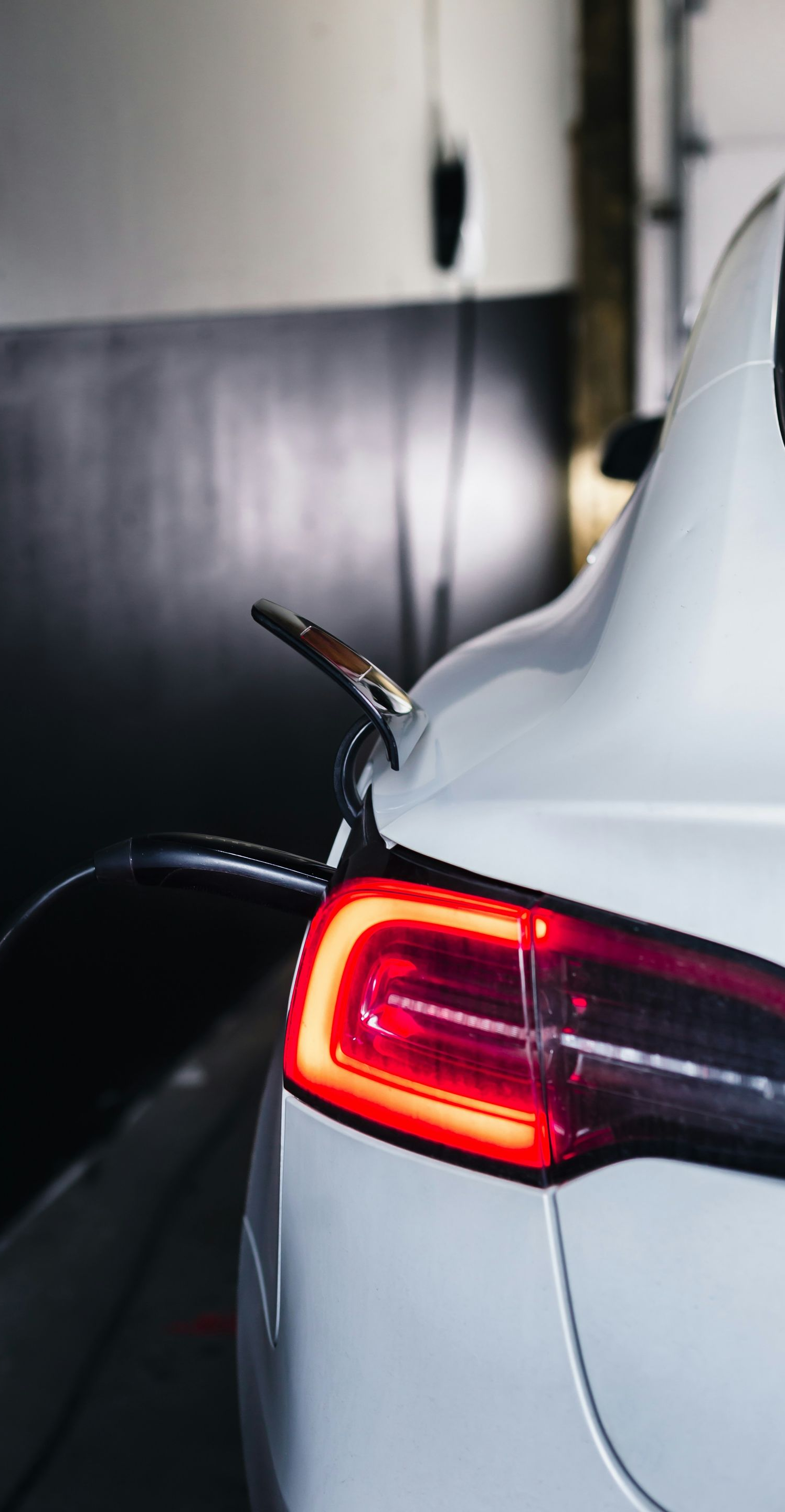 White electric car charging in a garage; red taillight illuminated, charging cable plugged in.