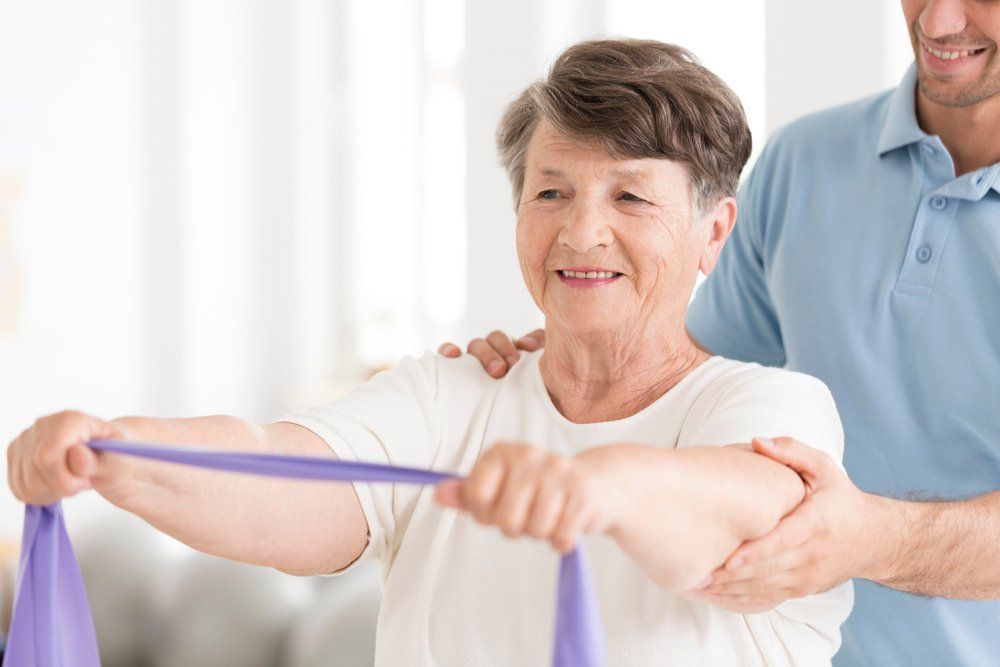 HaPpy Senior Woman Stretching With Elastic Tape During Rehabilitation — PhysioCare Townsville In Thuringowa Central, QLD