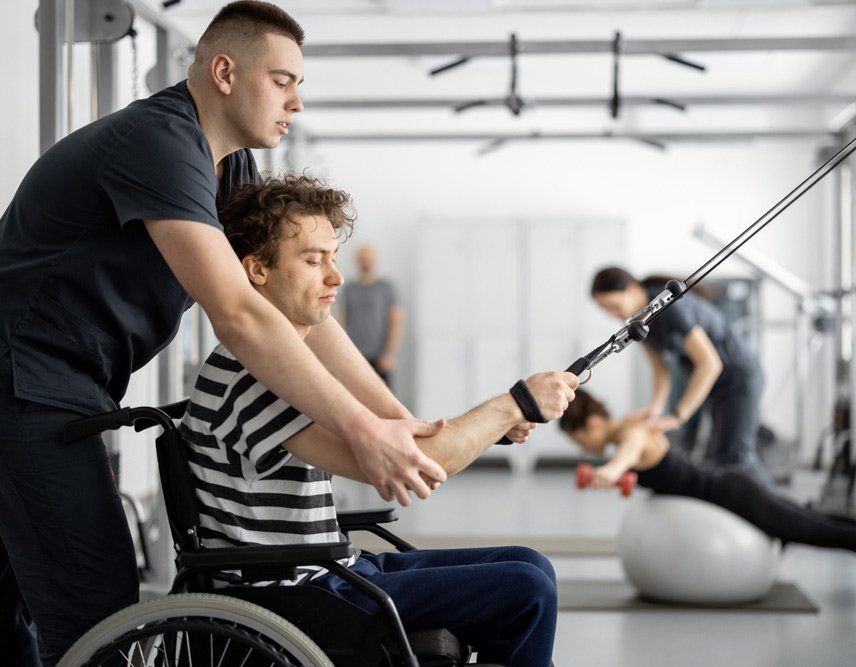 Rehabilitation Specialist Helps a Guy in a Wheelchair to Do Exercise for Recovery From Injury — PhysioCare Townsville In Thuringowa Central, QLD