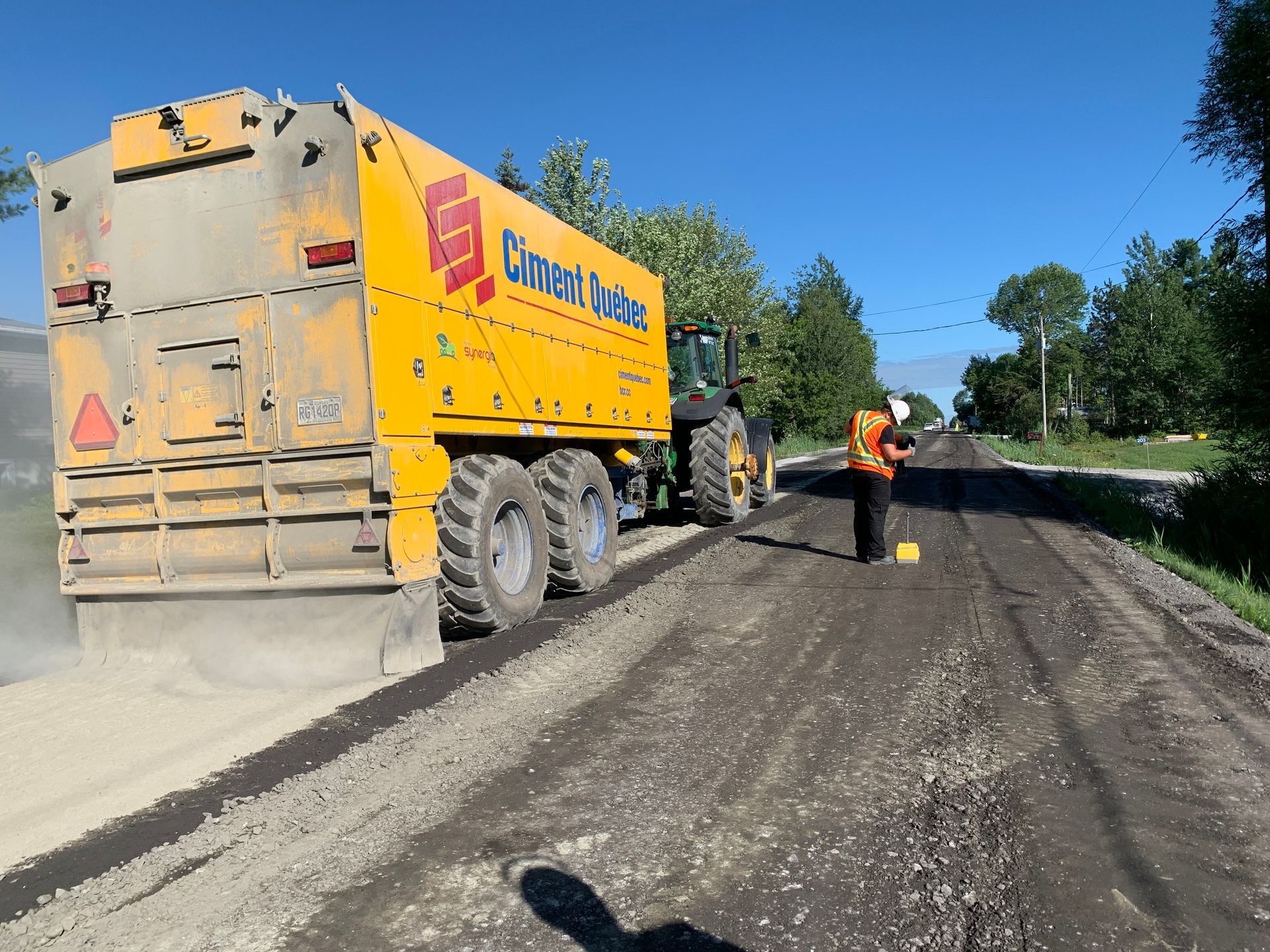 Machine de resurfaçage de route jaune sur une route, un ouvrier debout à proximité.