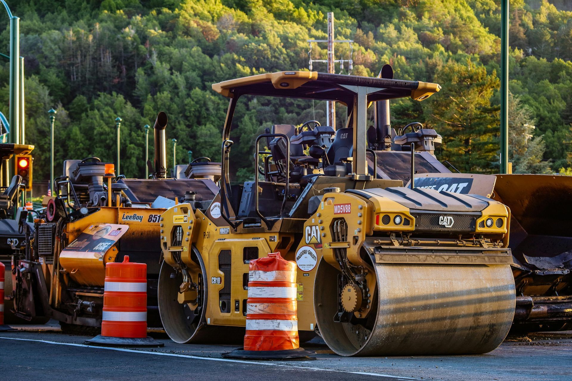 Rouleau compresseur jaune et autres véhicules de construction sur une route, avec des cônes de signalisation orange.