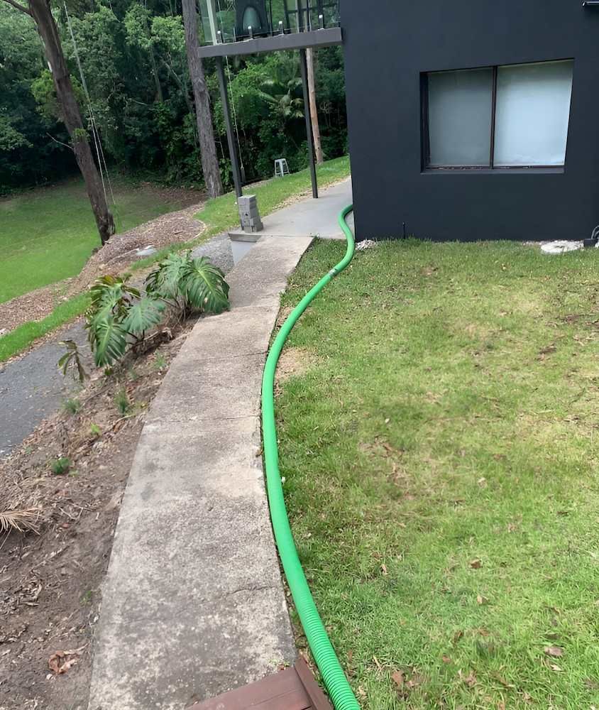 A Green Hose is Connected to a Sidewalk Next to a House — Glenview Septic & Liquid Waste Removal In Glenview, QLD