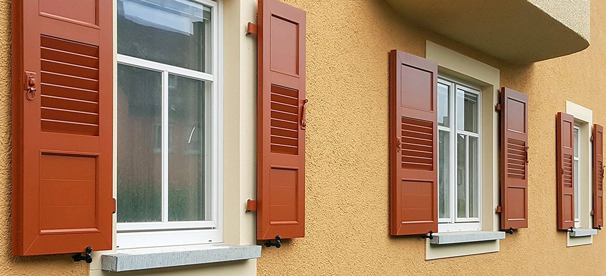 Eine Reihe von Fenstern mit roten Fensterläden an einem Gebäude.