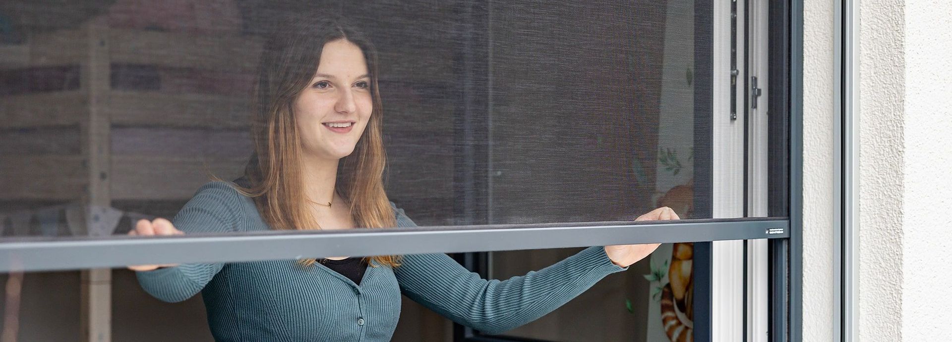 Eine Frau schaut aus einem Fenster mit Fliegengitter.