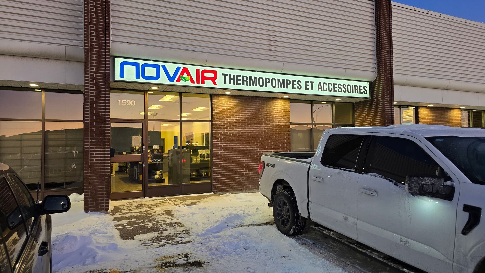 Façade enneigée avec une enseigne « novair » et une camionnette blanche garée devant au crépuscule