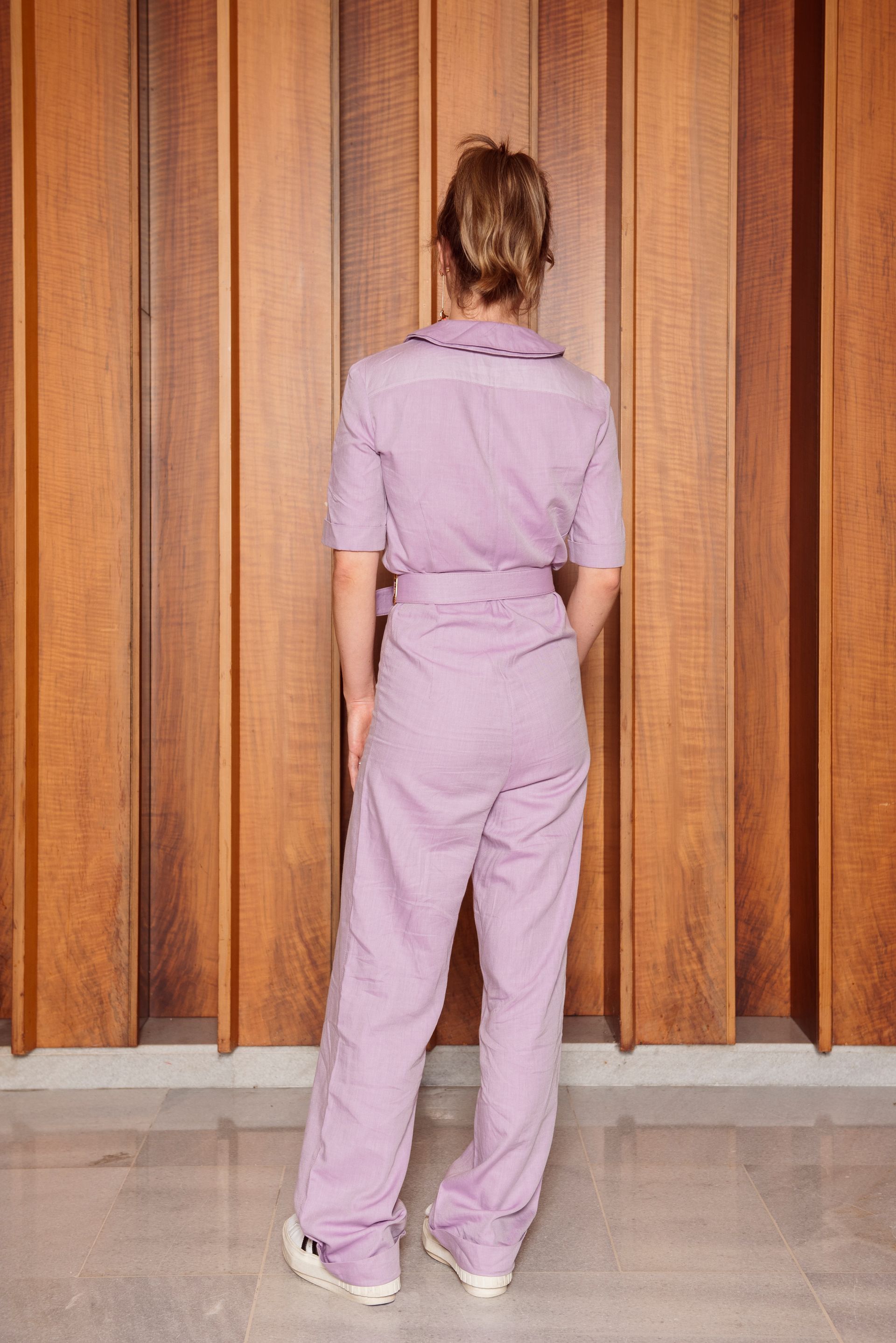 Een vrouw in een paars overall staat voor een houten wand.