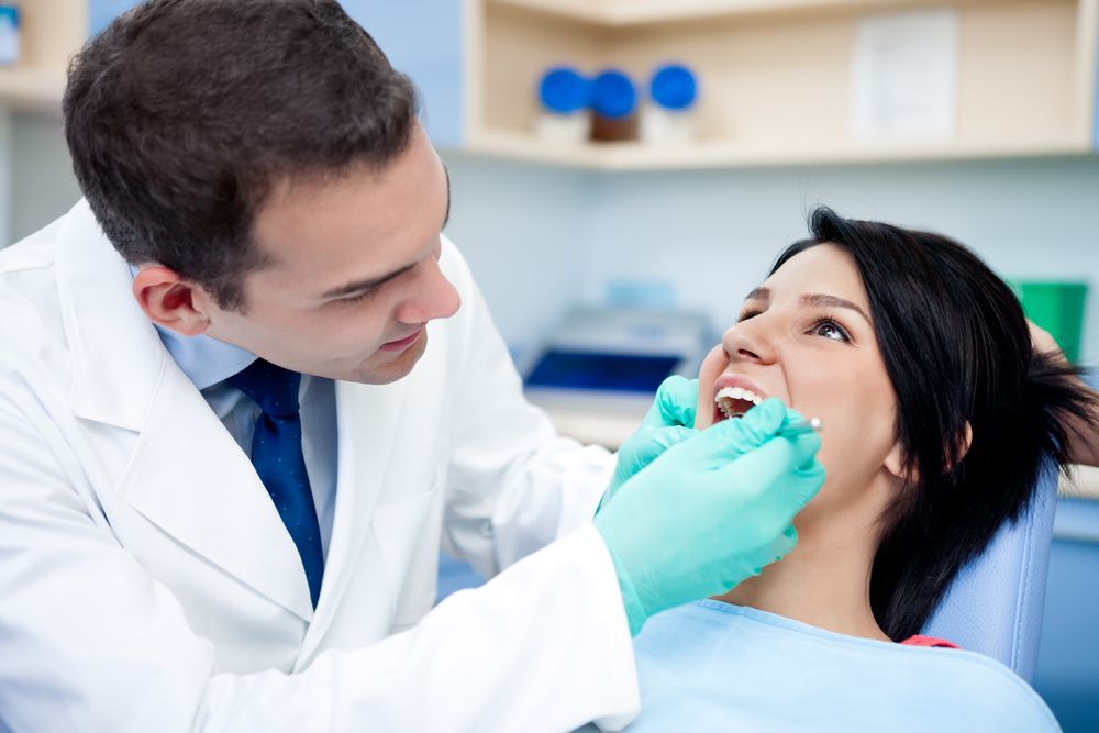 Dentist examining a woman's teeth in an office. He wears a white coat and gloves. Woman smiles.  — Coronation House Dentist in Nambour, QLD