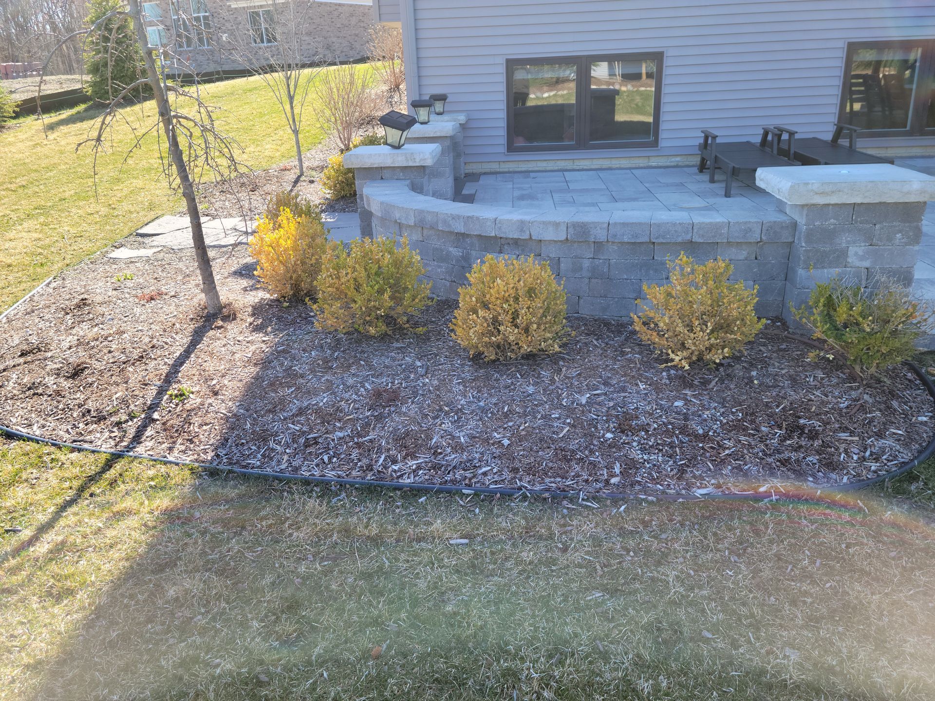 A gravel path with wooden steps winds through a landscaped garden filled with various evergreens, shrubs, and large rocks.