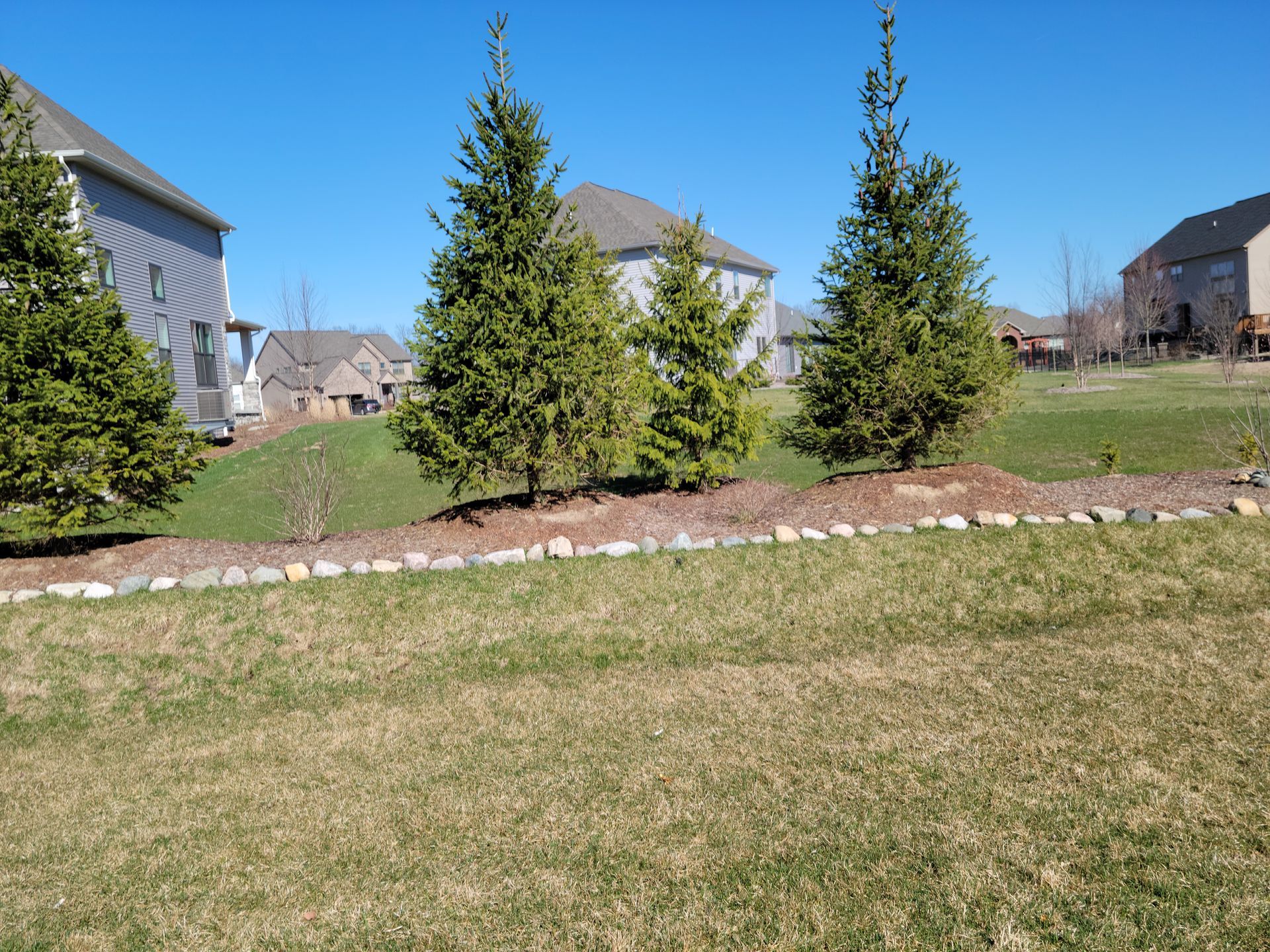 A landscape worker in a high-visibility vest tends to a potted plant on a patio, with another worker visible in the garden.