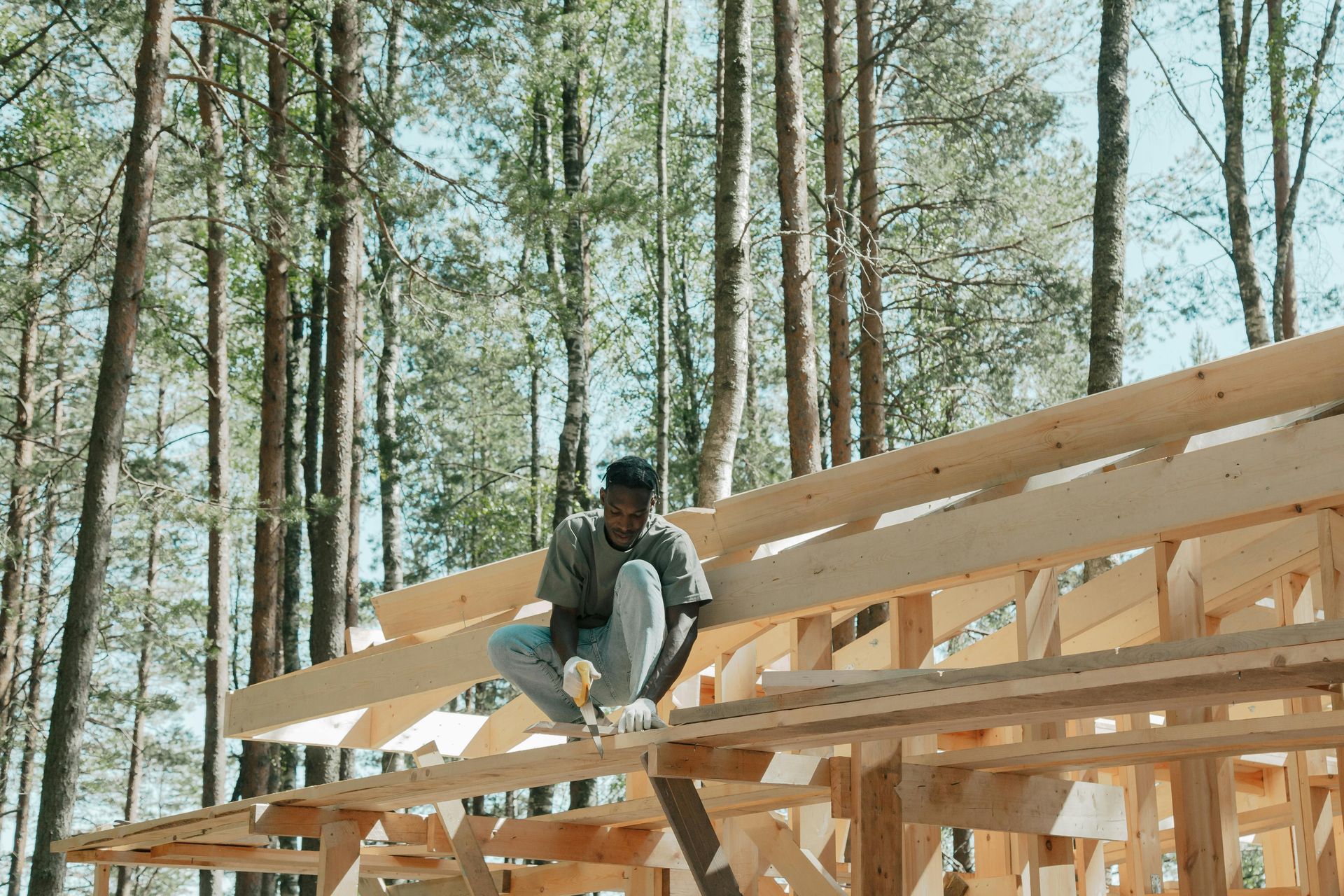 Person on wooden roof frame in a forest, working on construction.
