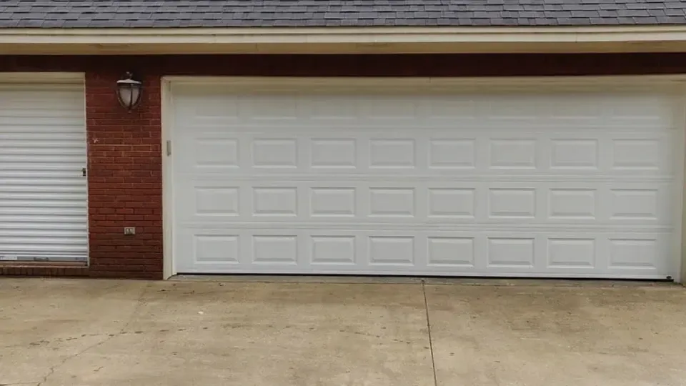 White garage door with panel design, adjacent to a brick wall and secondary door.