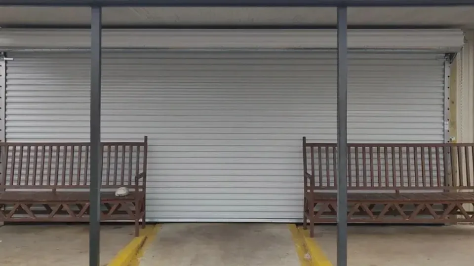 Two wooden benches flank a closed, gray roll-up door. A loading dock with yellow lines is in front.