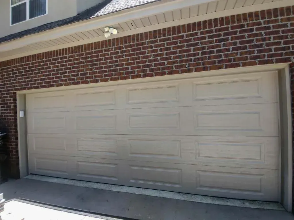 Tan garage door in front of a brick building.
