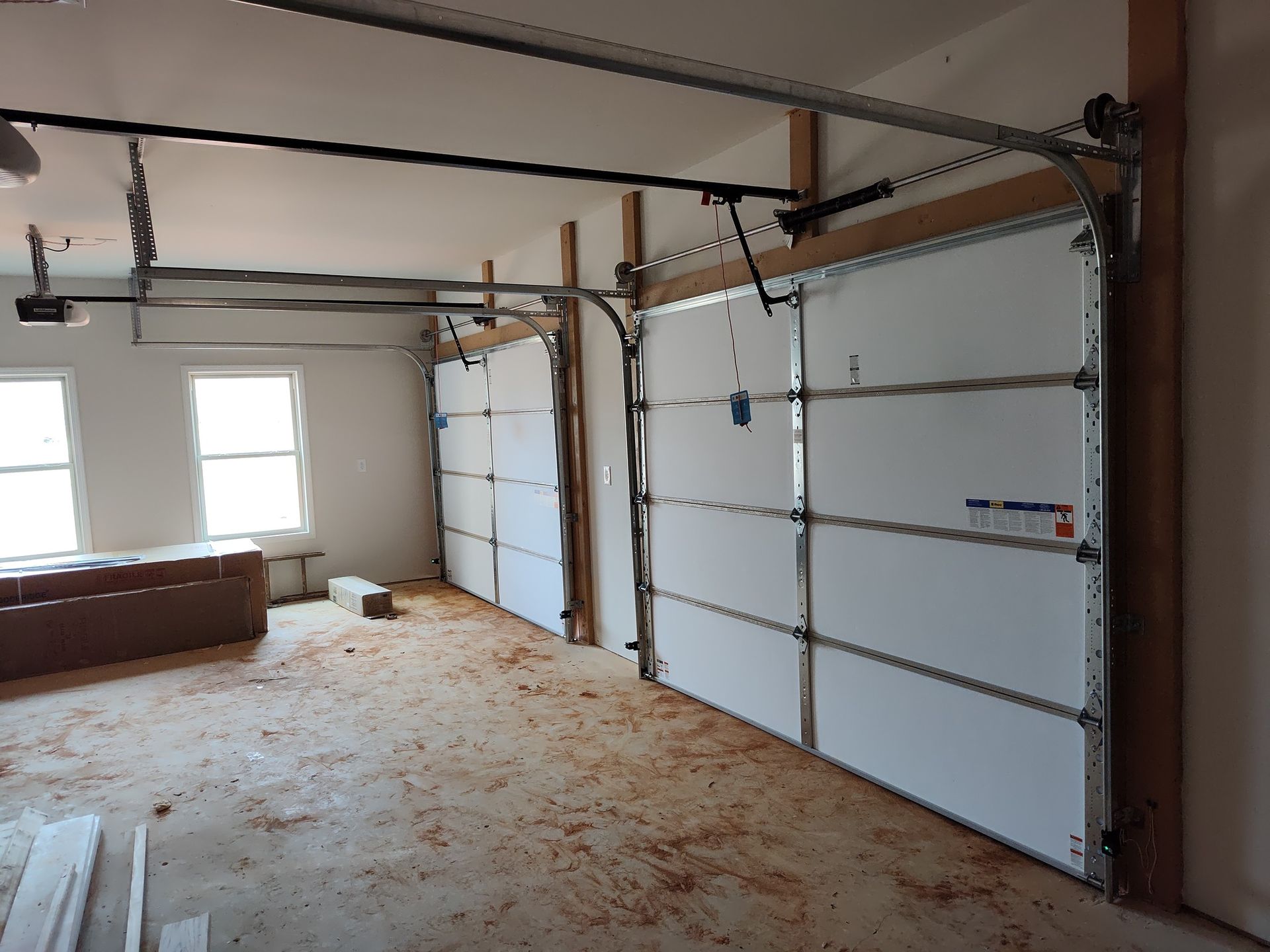 Garage interior with two white garage doors, unfinished floor, and construction debris.