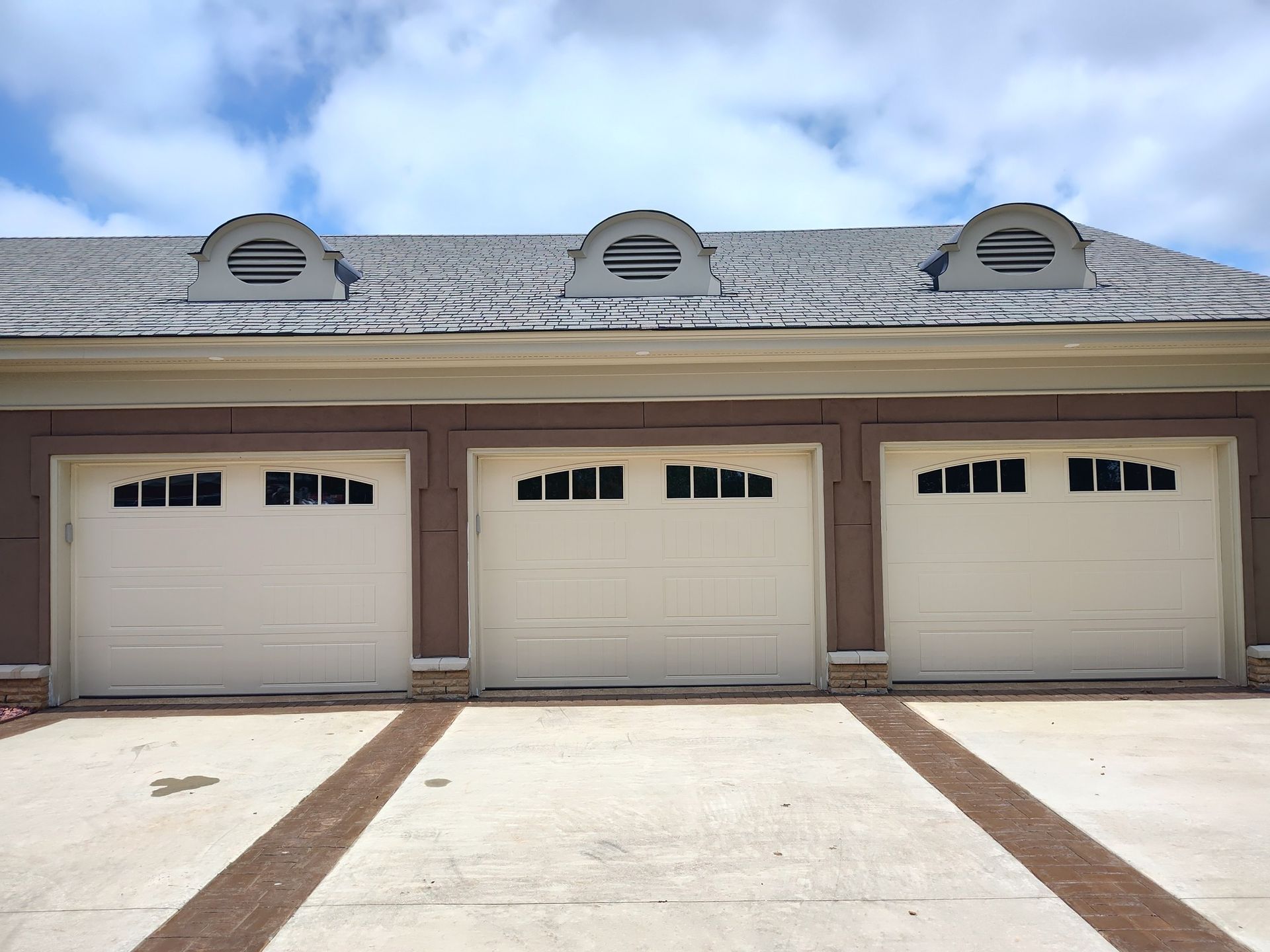 Three white garage doors with arched windows, tan trim, and oval roof vents; driveway in front.