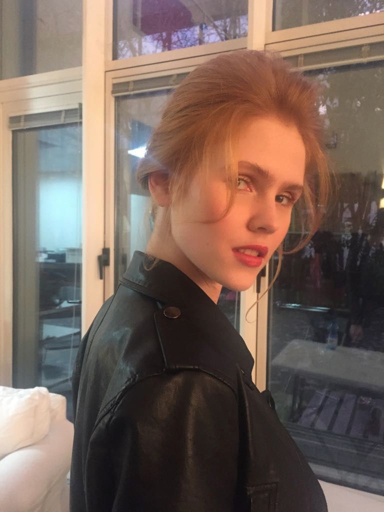 Una donna con una giacca di pelle nera è in piedi davanti a una finestra.