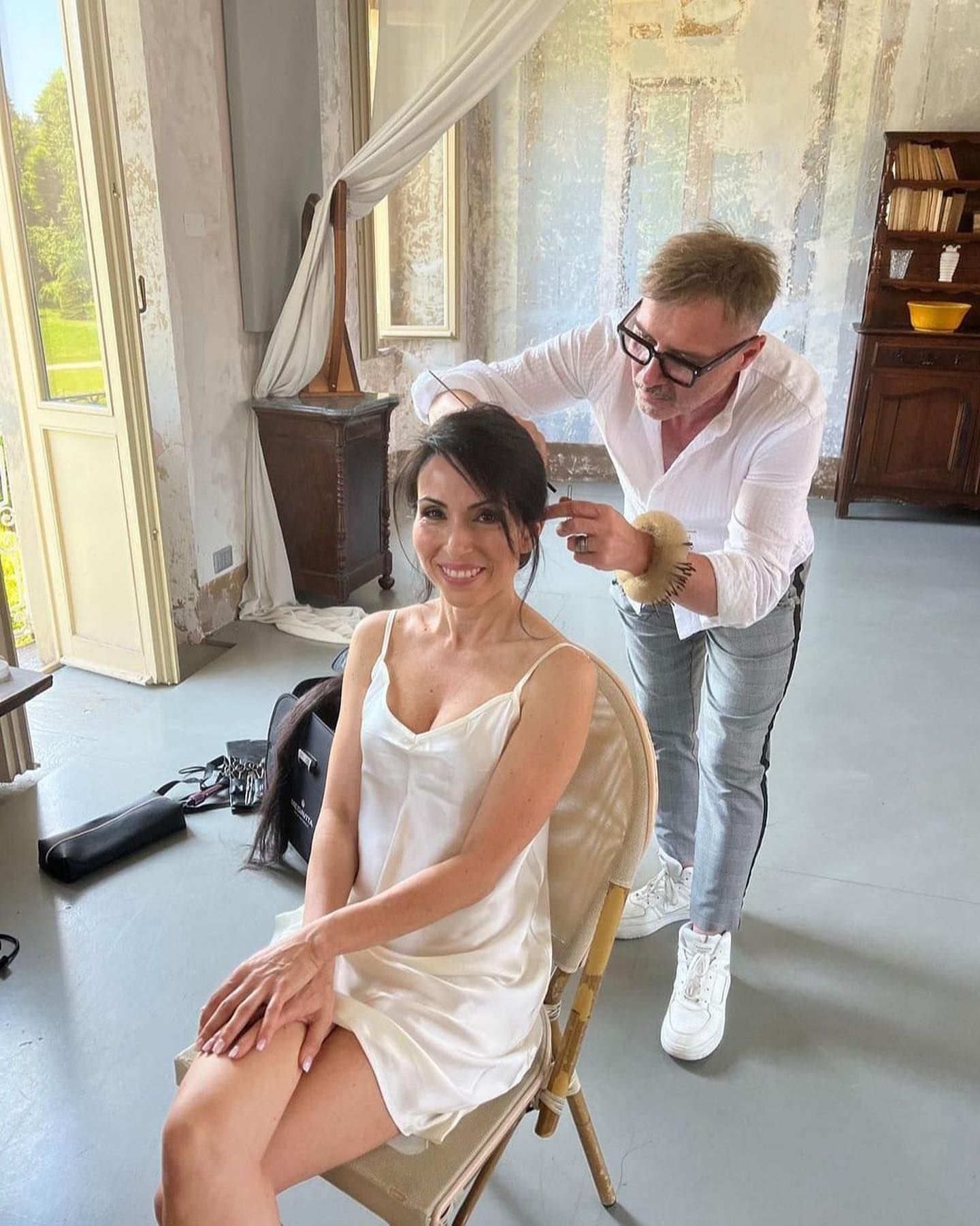 Una donna vestita di bianco è seduta su una sedia mentre un uomo le spazzola i capelli.