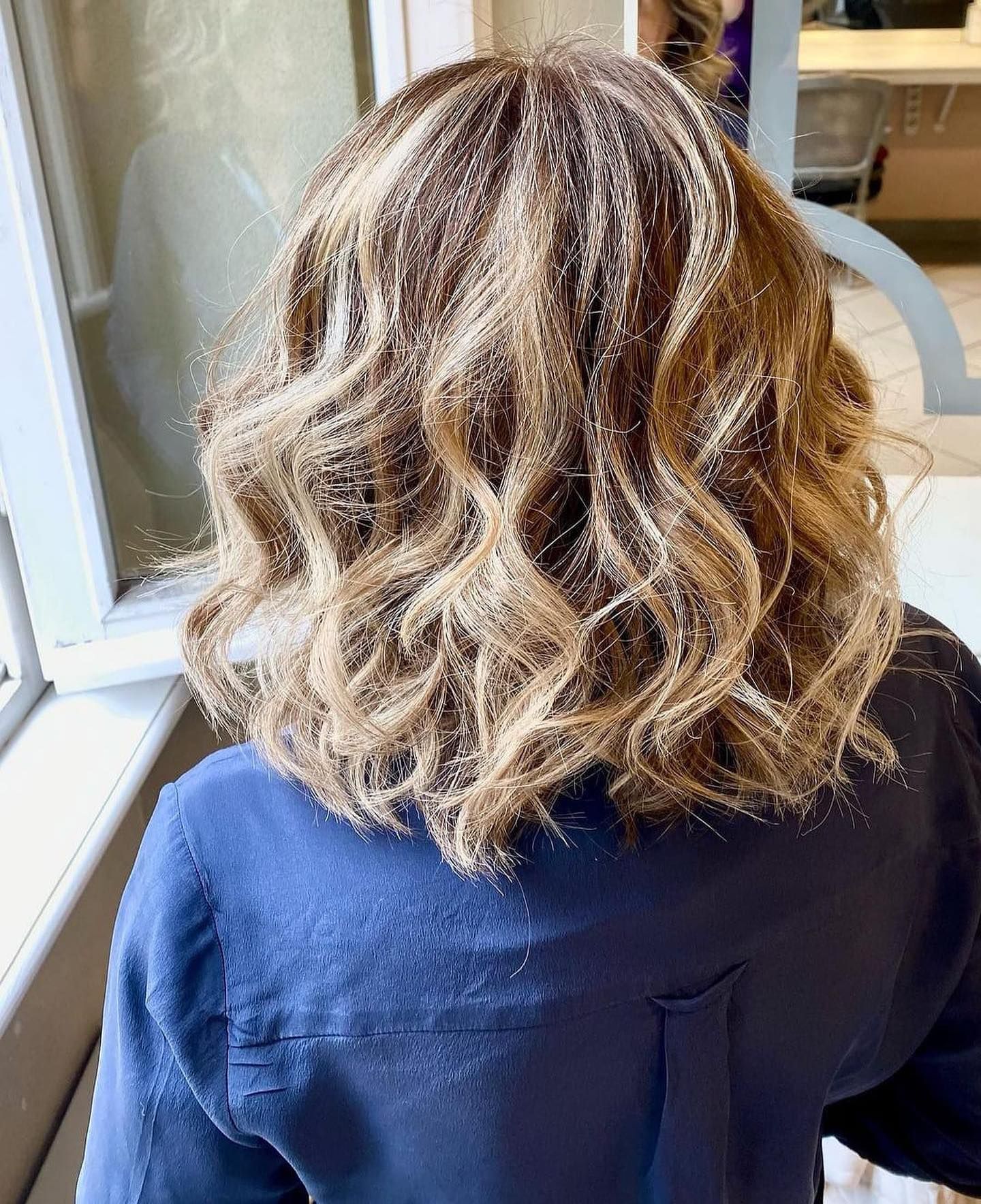 Una donna con i capelli ricci è seduta davanti a una finestra.