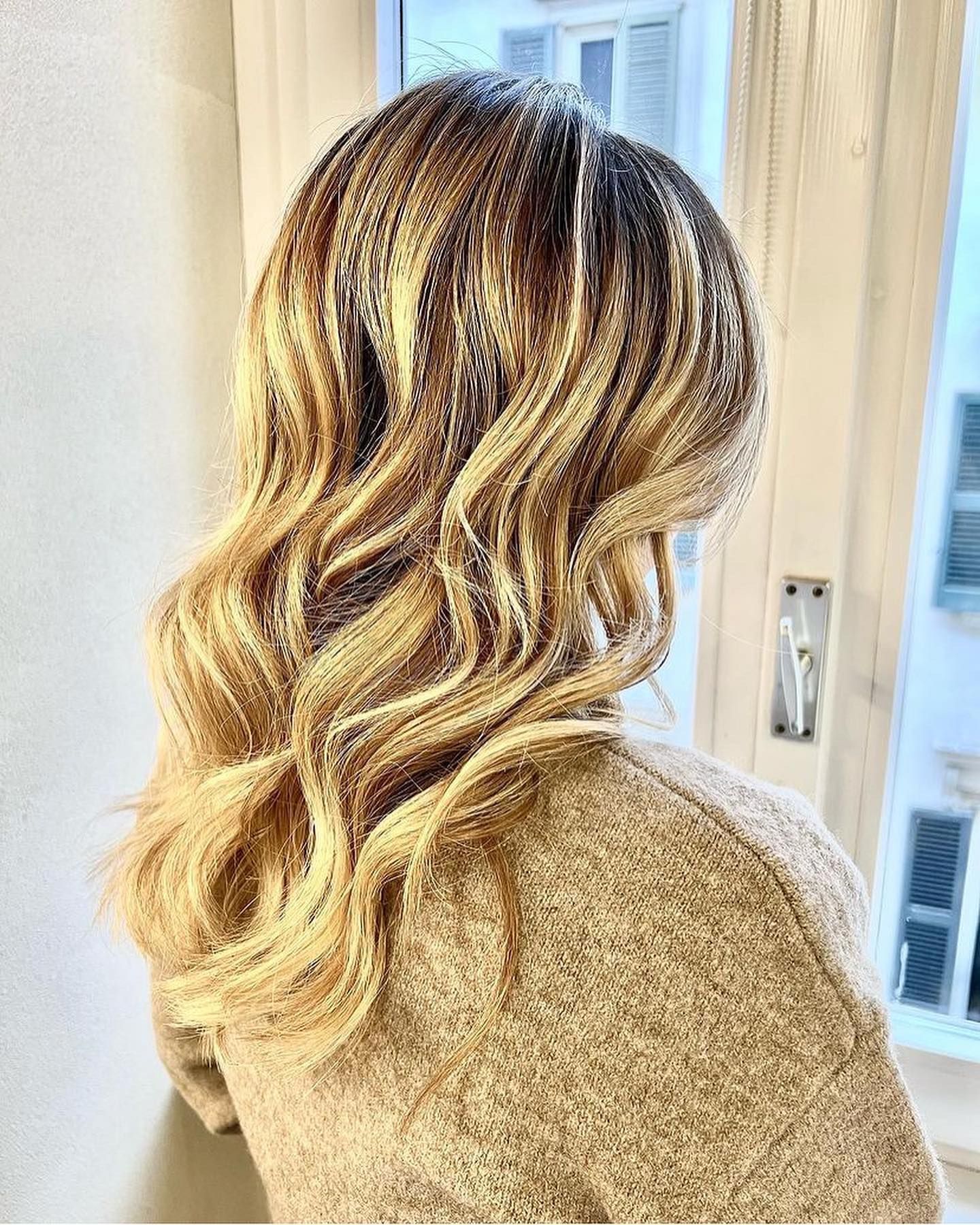 Una donna con lunghi capelli biondi è in piedi davanti a una finestra.