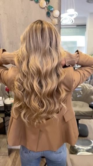 Una donna con lunghi capelli biondi è in piedi in una stanza con le mani nei capelli.