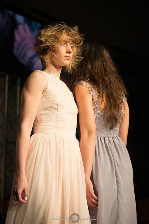 Due donne in abito elegante sono in piedi una accanto all'altra su un palco.