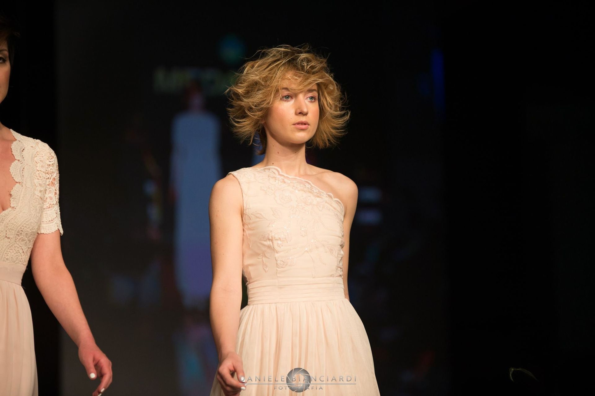 Una donna in abito bianco sta sfilando sulla passerella durante una sfilata di moda.