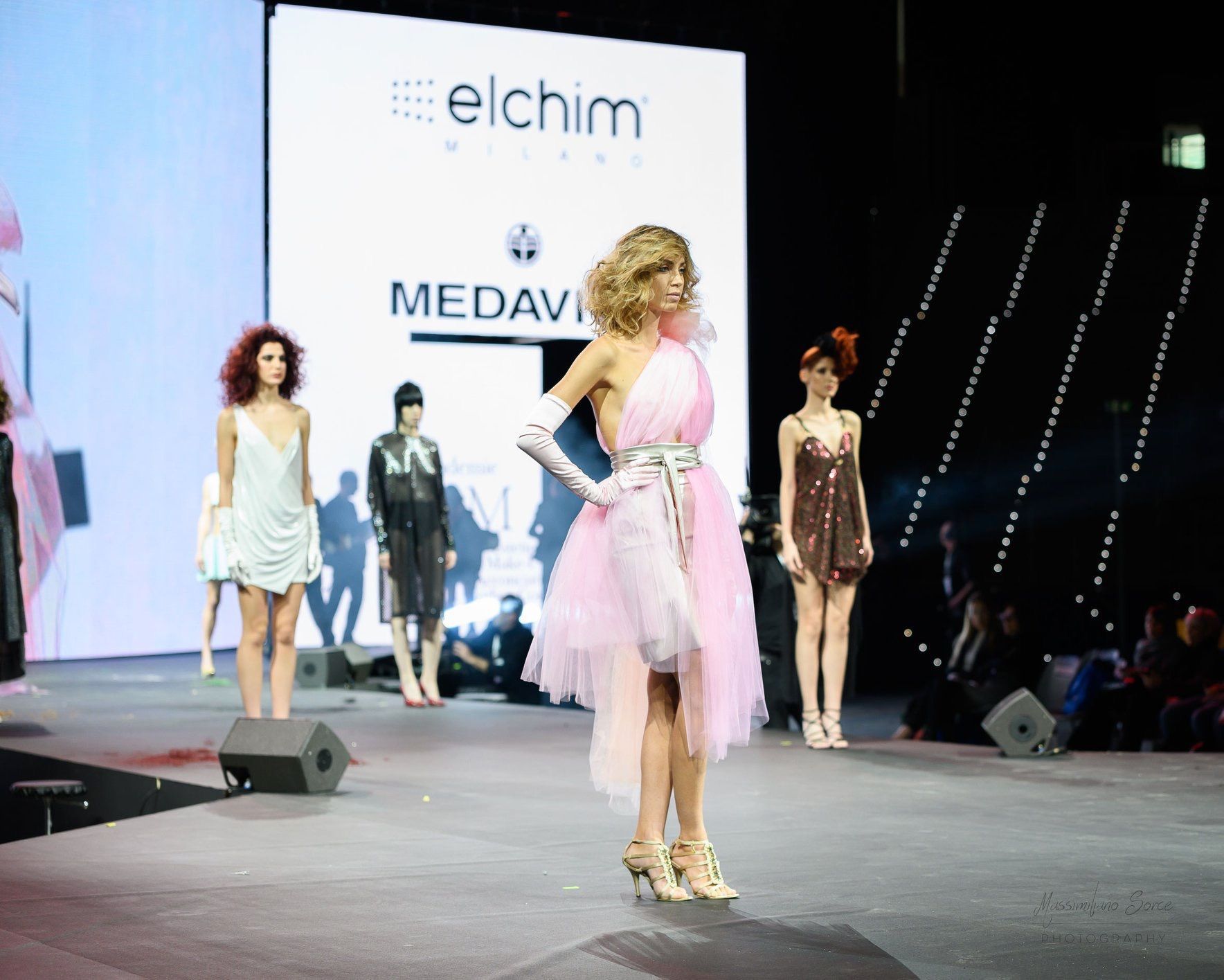 Una donna con un vestito rosa sta sfilando sulla passerella durante una sfilata di moda.