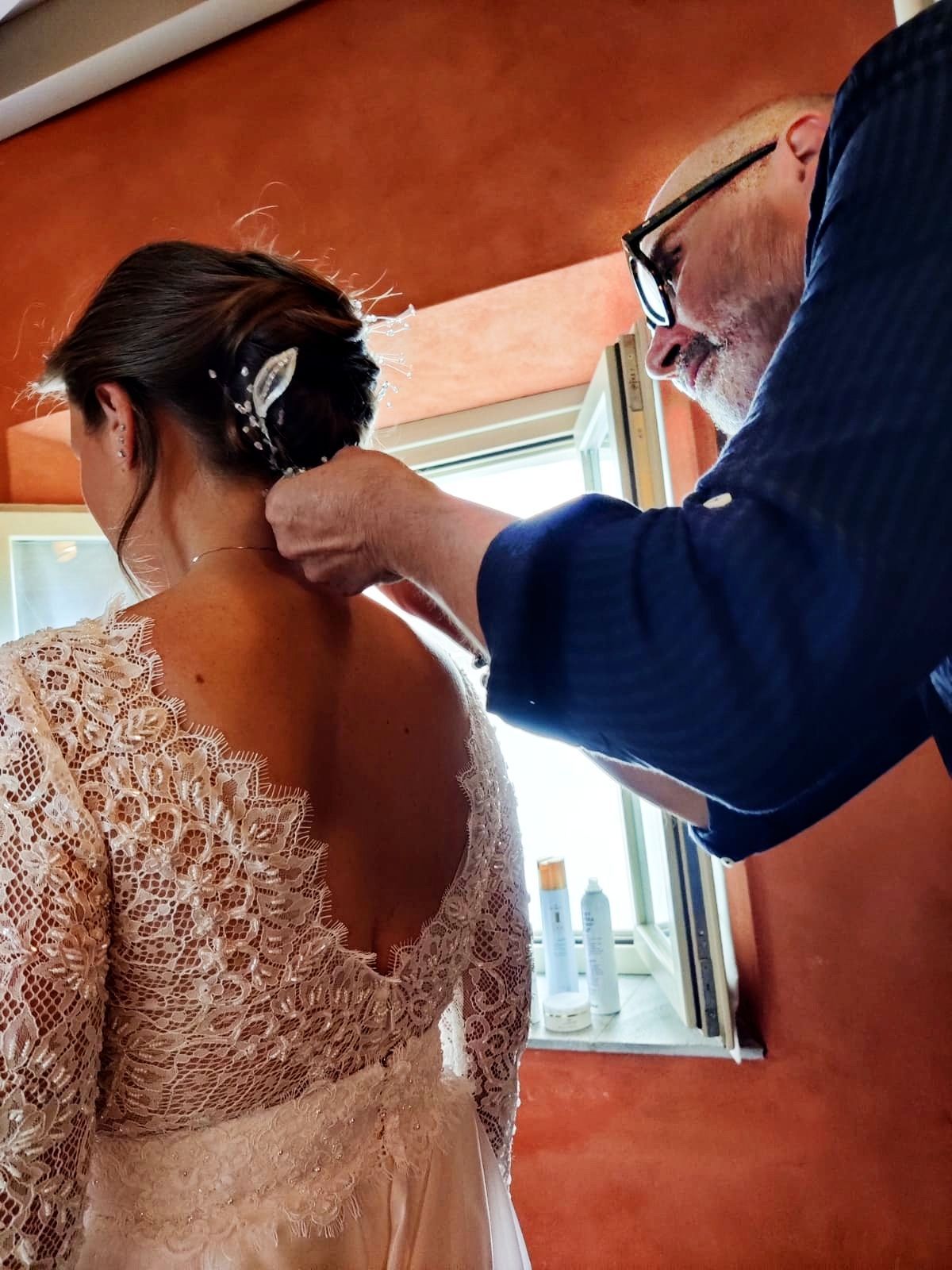 Una donna in abito da sposa si fa fare i capelli da un uomo
